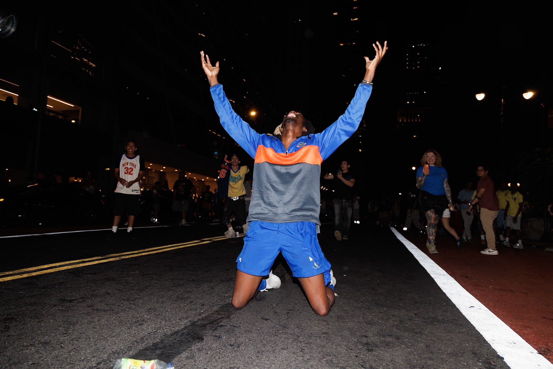 Kneeling Figure Raises Arms in Nighttime Street Celebration