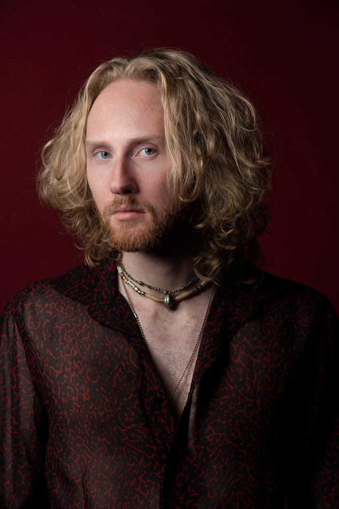 studioportret van gitarist Theo van Niel Jr voor een rode achtergrond