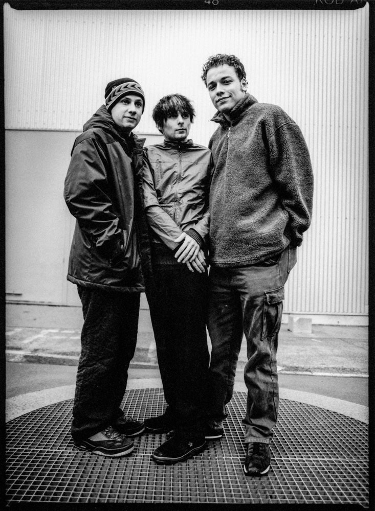 Zwartwit portret van Muse, een Britse rockband uit Teignmouth die in 1994 is opgericht. De band bestaat uit zanger, gitarist en pianist Matthew Bellamy, drummer Dominic Howard en bassist Christopher Wolstenholme. Gefotografeerd in Den Haag in 1999 door Michel Mees.