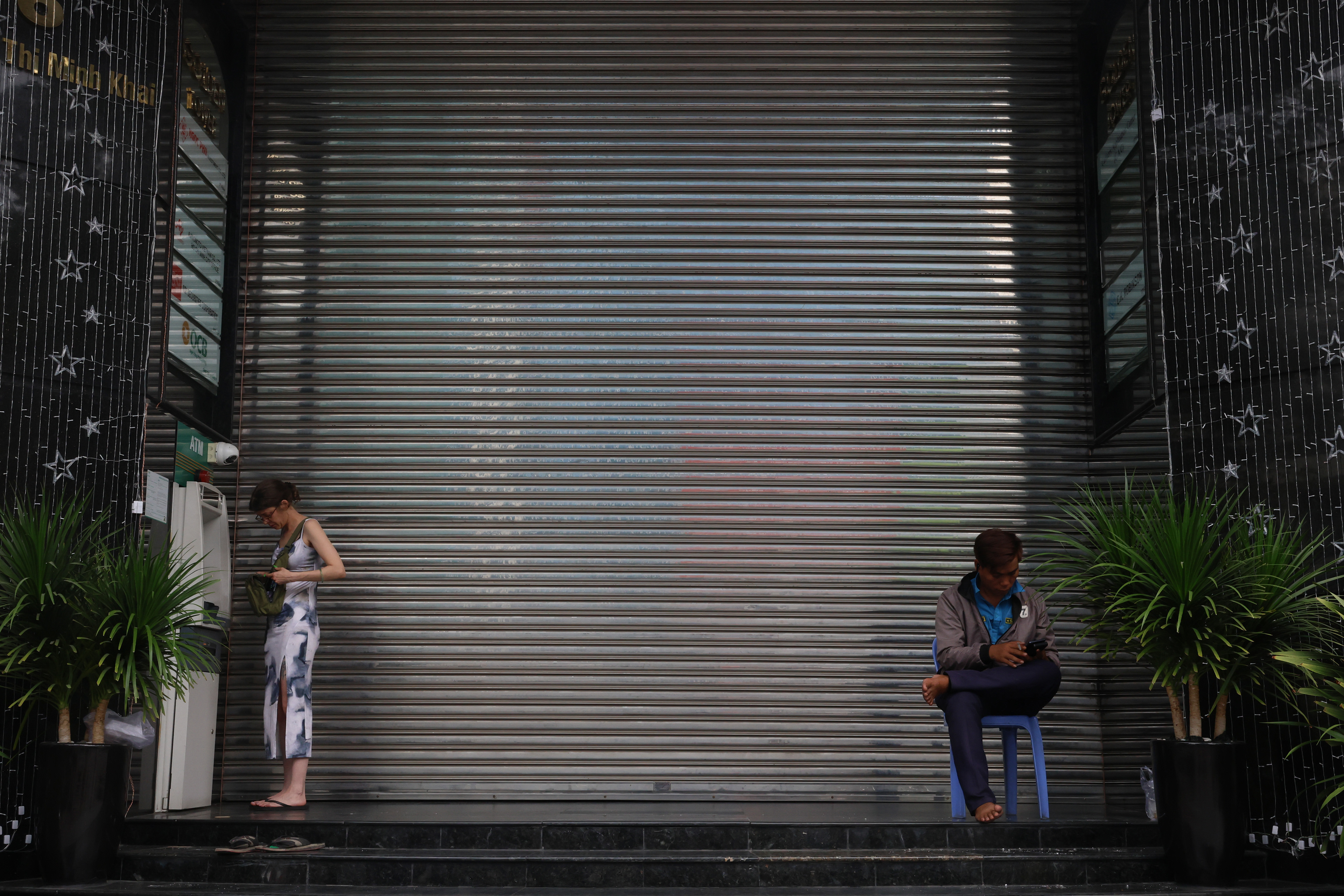 A woman digs through her purse in front of an ATM across from a security guard at the front gate of an office building in Ho Chi Minh City, Vietnam on Wednesday, Jan. 1, 2025. The building serves as a headquarters for many major companies, including Ajinomoto food service, Ngoc Phu Investment, SSI Security and OCB stock trading.