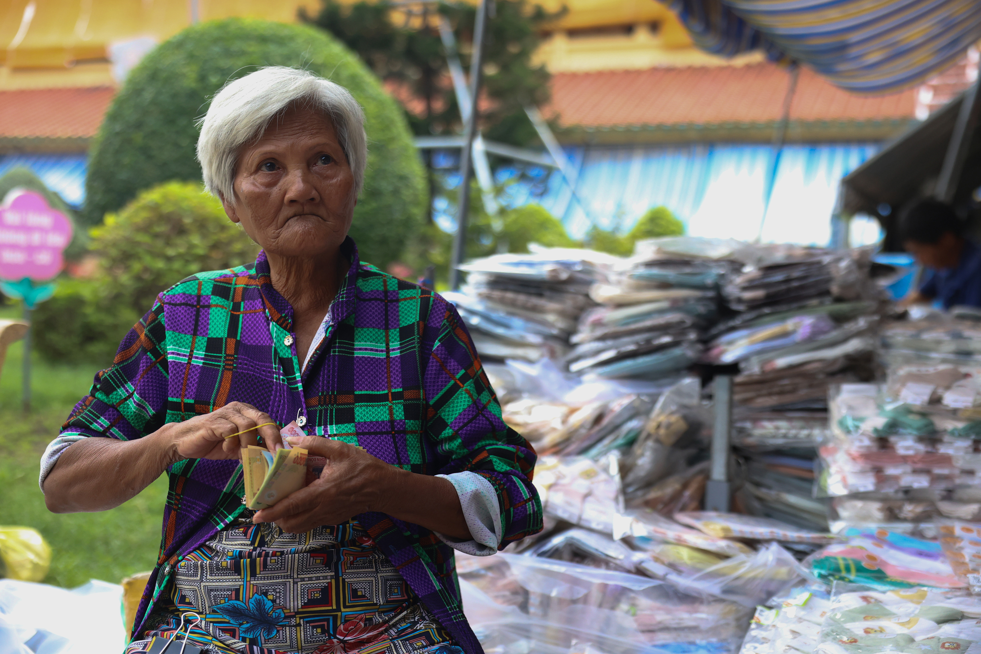 A vendor sits in front of her merchandise, souvenir t-shirts, counting her money on Thursday, January 2, 2025 in the Binh Tay market in Ho Chi Minh City, Vietnam.