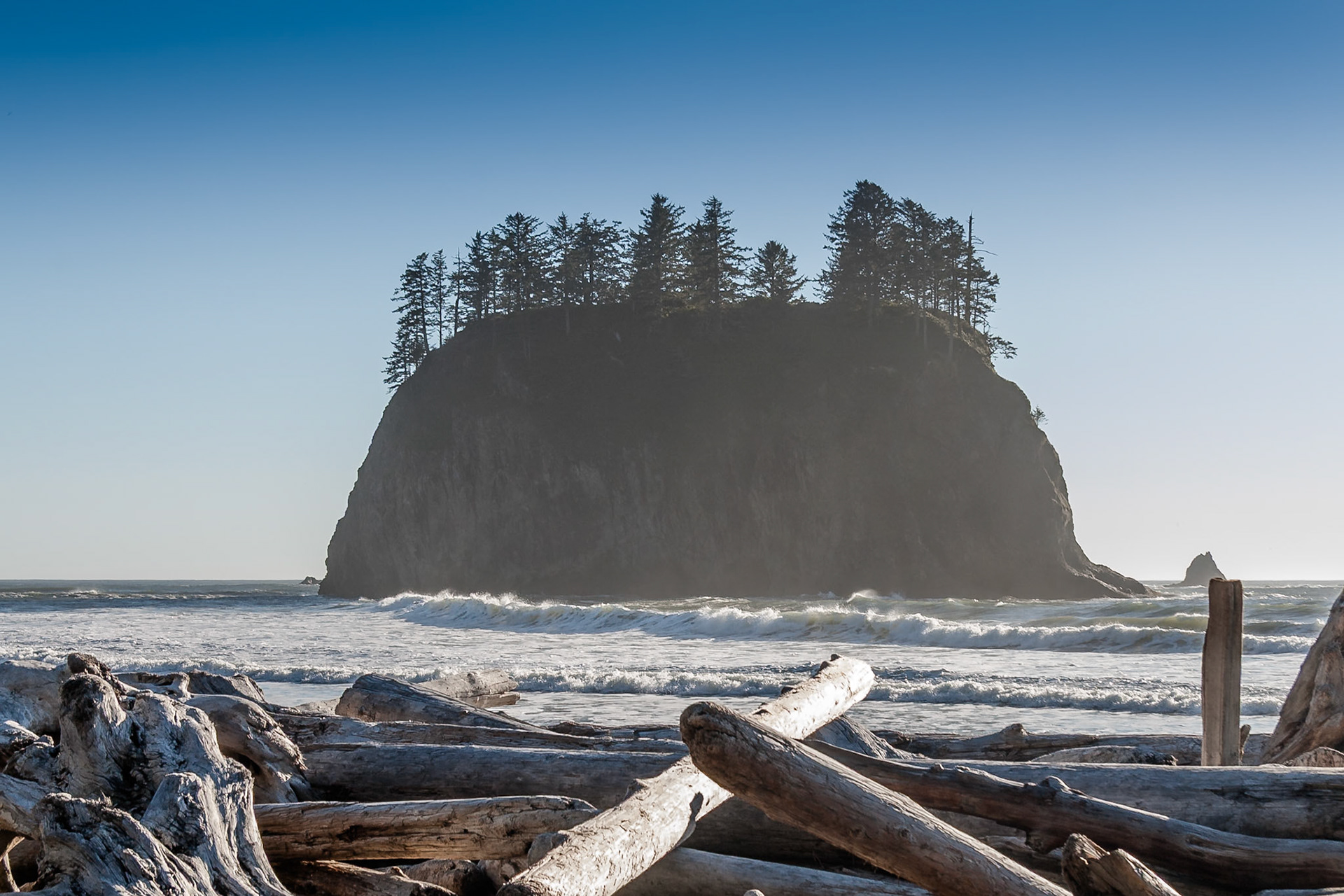 Driftwood at the shore at Second Beach with big rock in the sea in the background near La Push, Olympic National Park, WA, USA