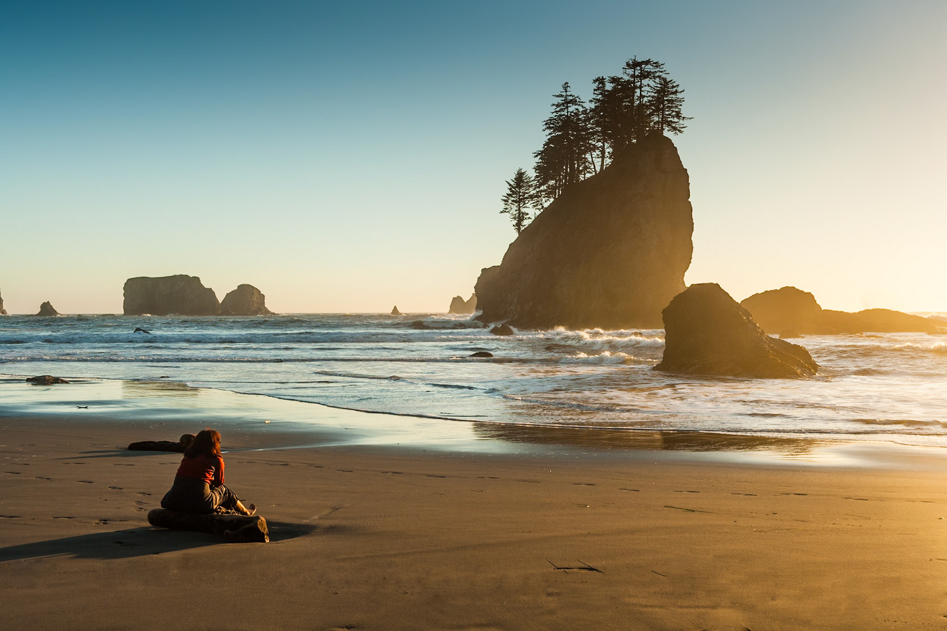 Woman sits on the Second Beach near La Push at the Olympic National Park at sunset, Washington, USA