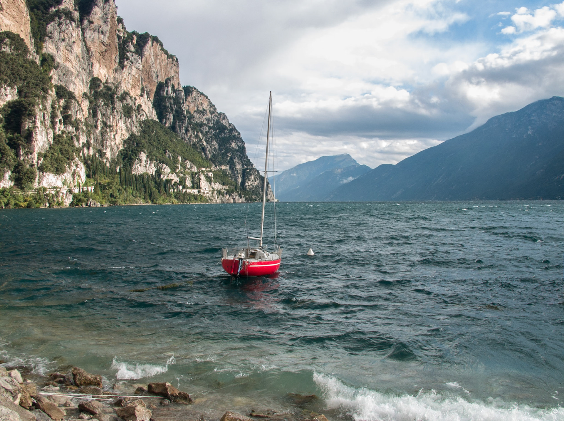 Windy lake Lago di Gardo with red sailing boat, Italy