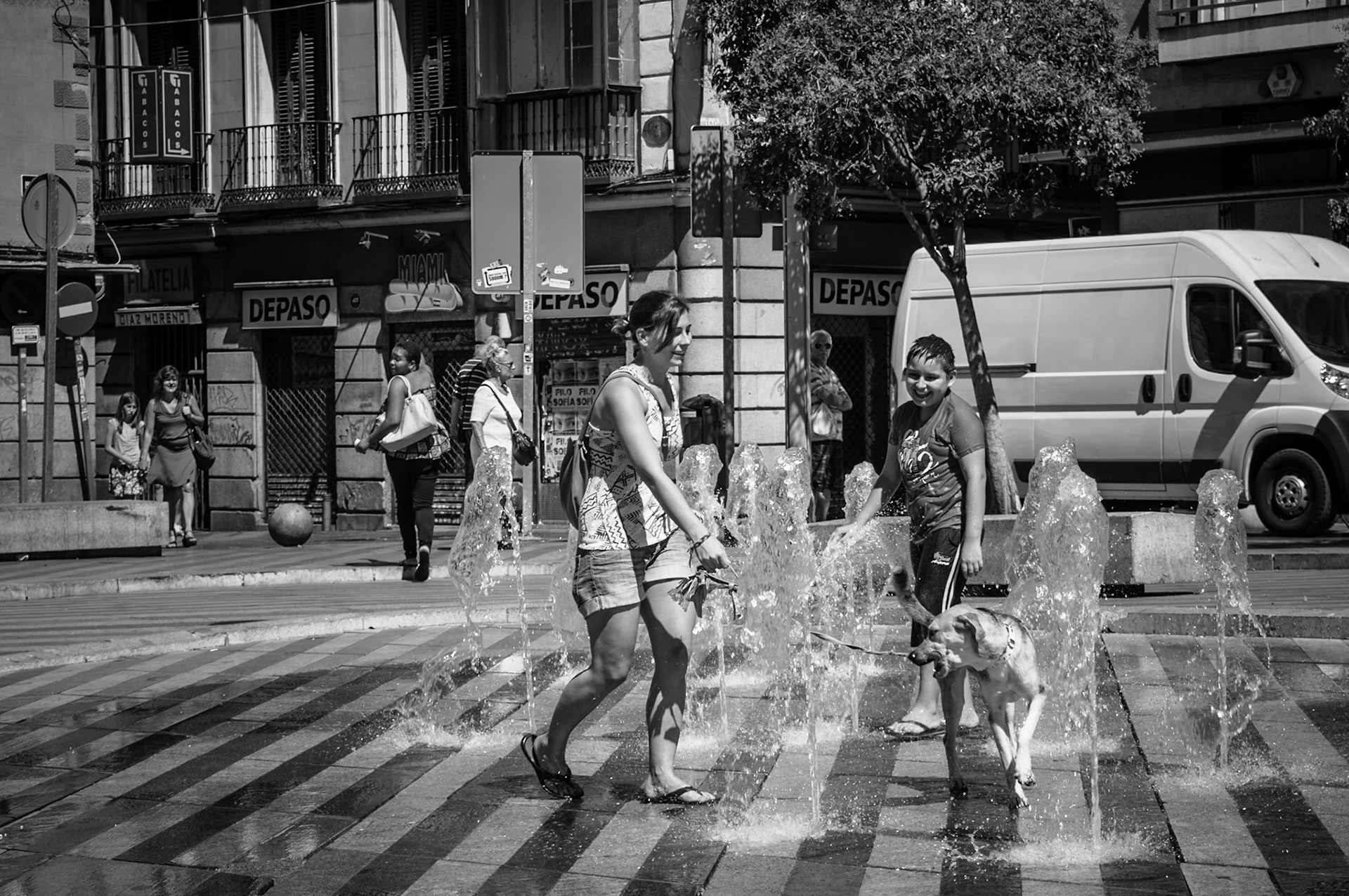 A girl with her dog cooling of in a play fountain in Madrid, Spain