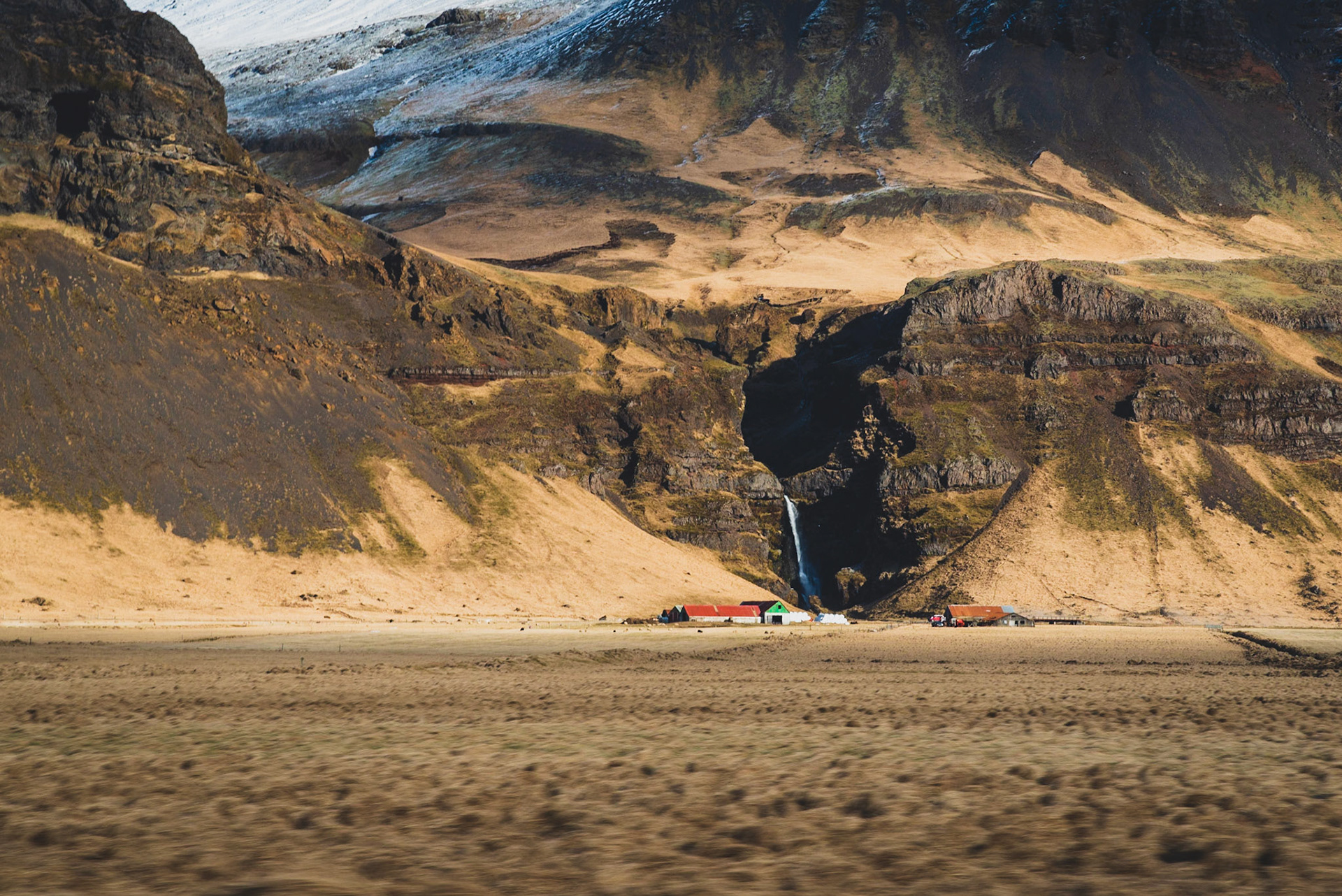 Icelandic landscape with a waterfall and farms, shot through the window of a moving car