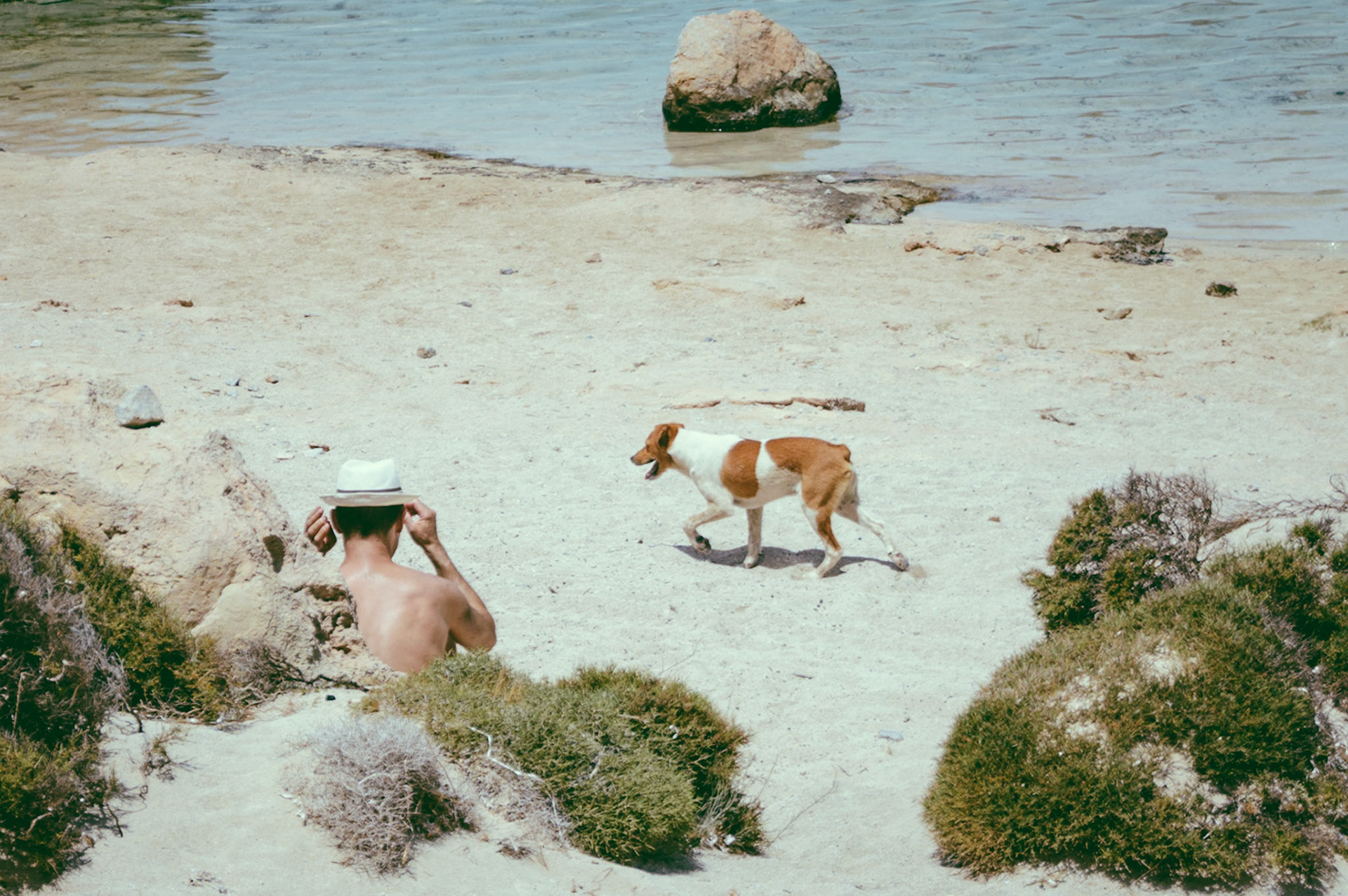 A man sunbathing while a dog is passing at Balos Beach, Crete, Greece