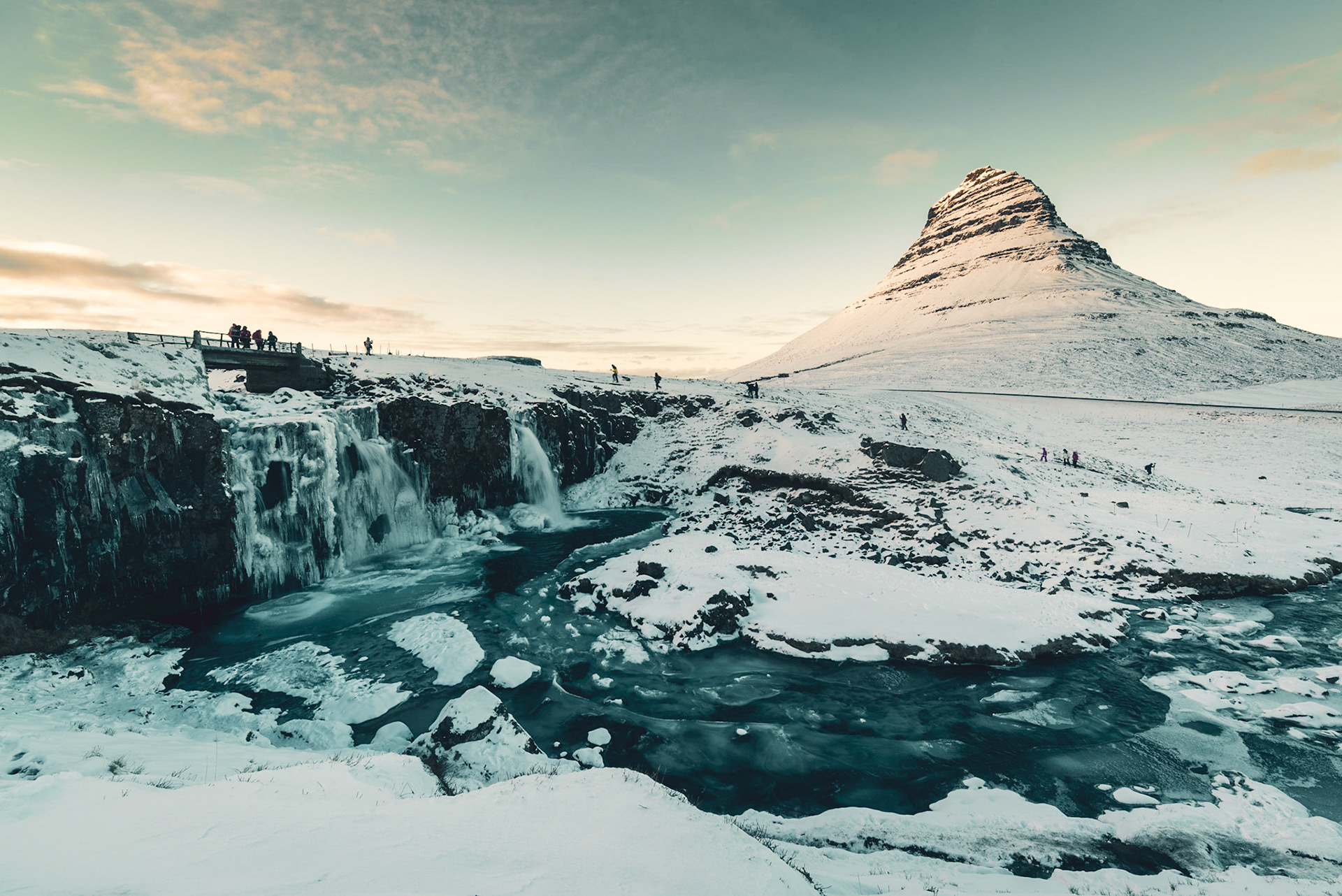 Kirkjufellsfoss waterfall with hikers and photographers under a cloudy Kirkjufell