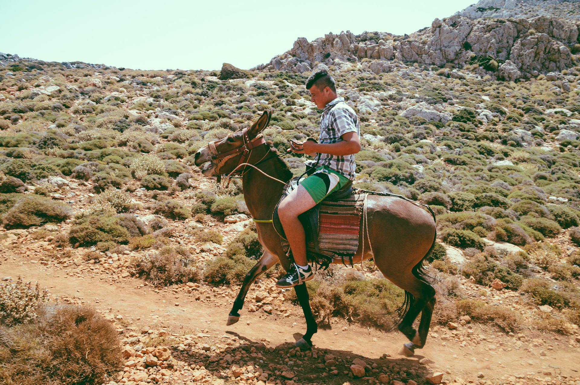 Boy riding a donkey at the trail towards Balo's beach in Crete, Greece