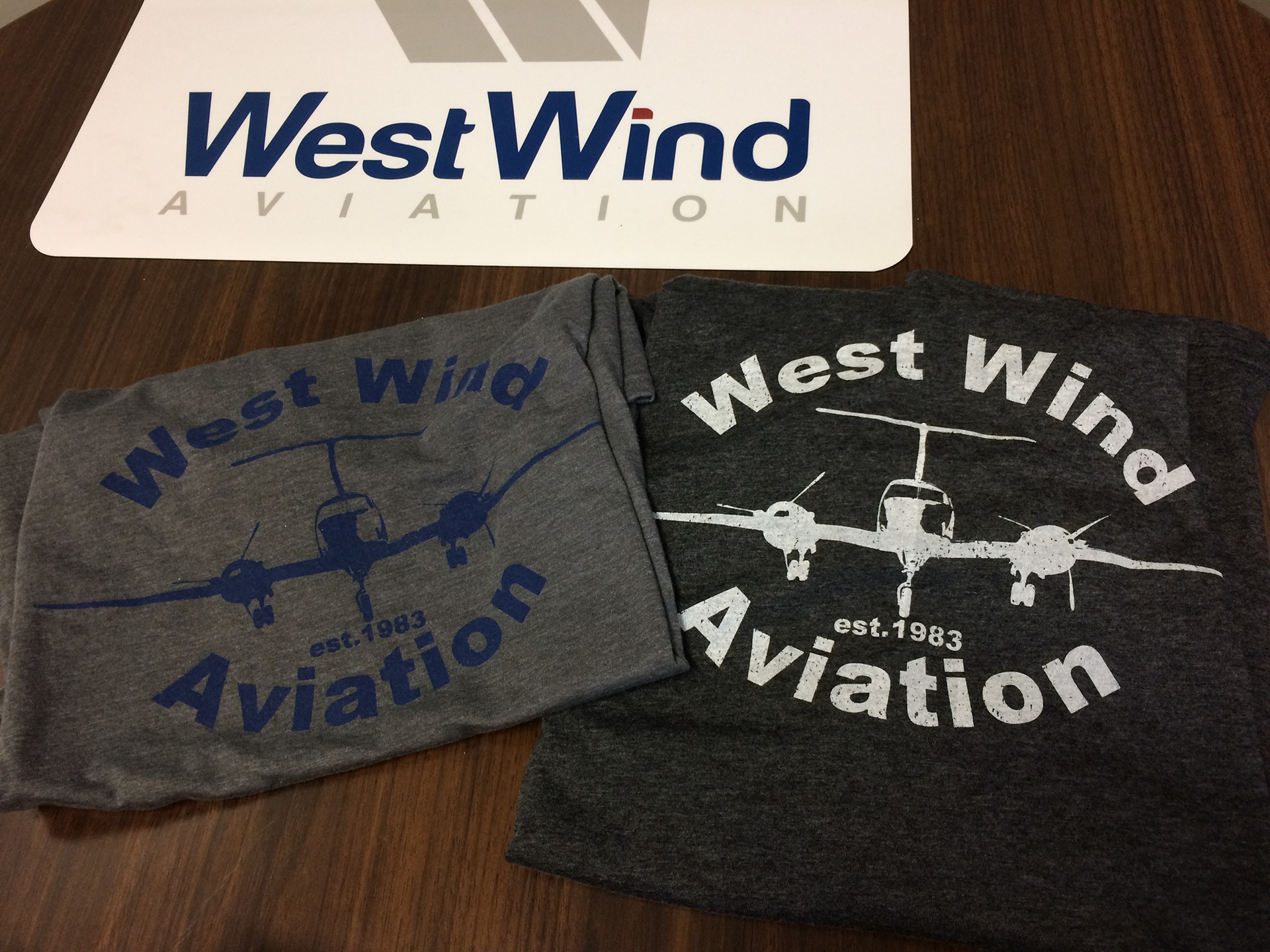 T-Shirts made to look like old camp shirts that feature West Wind aviations First aircraft and the year it was established.