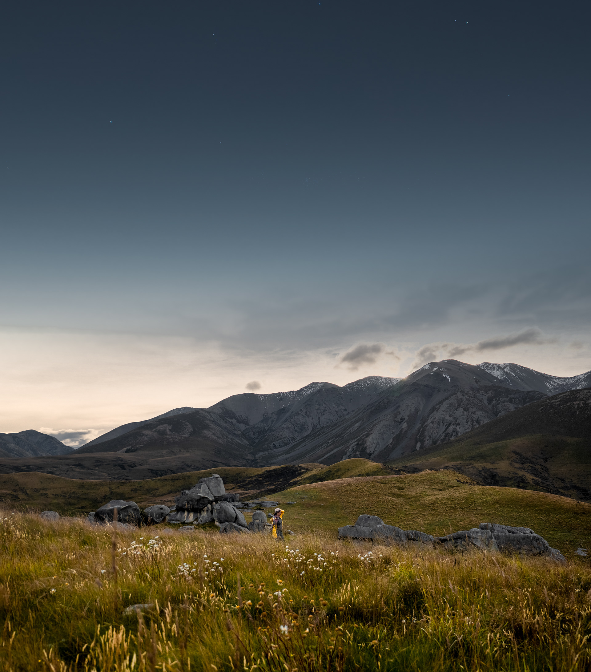 Hiker walking through tussock and limestone rock formations beneath the Southern Alps in New Zealand