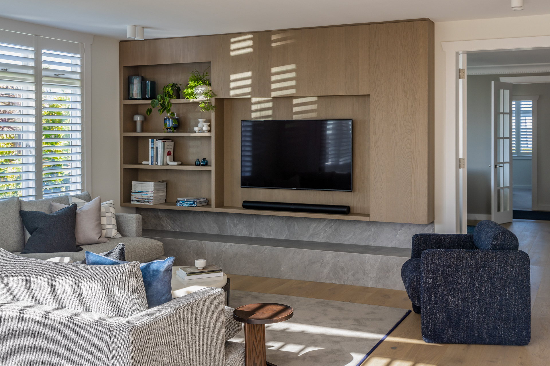 Codrington Residence living room with custom timber media wall, shelving and sunlight patterned through shutters