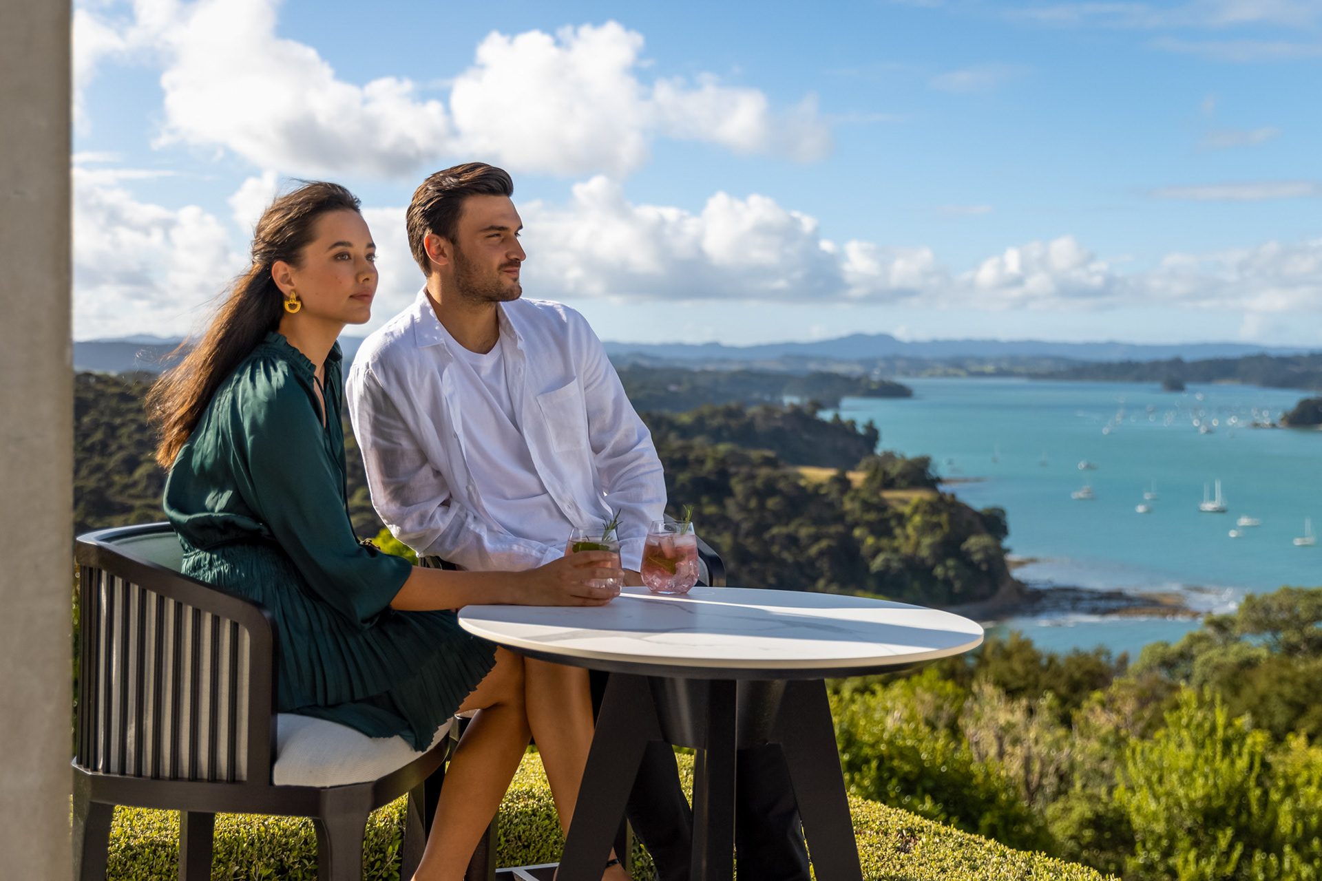 Lifestyle portrait of a couple enjoying drinks on a terrace overlooking a coastal New Zealand landscape