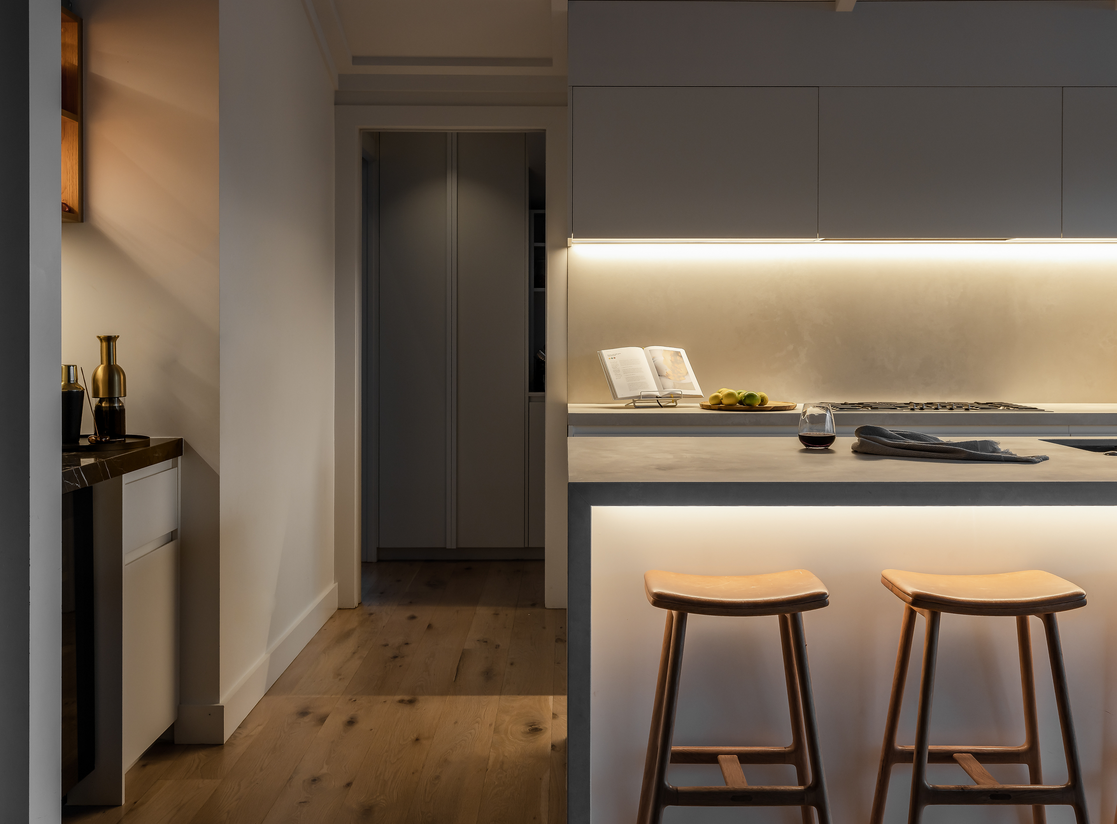 Evening detail of the Remuera bungalow kitchen with illuminated cabinetry, island seating and warm ambient light