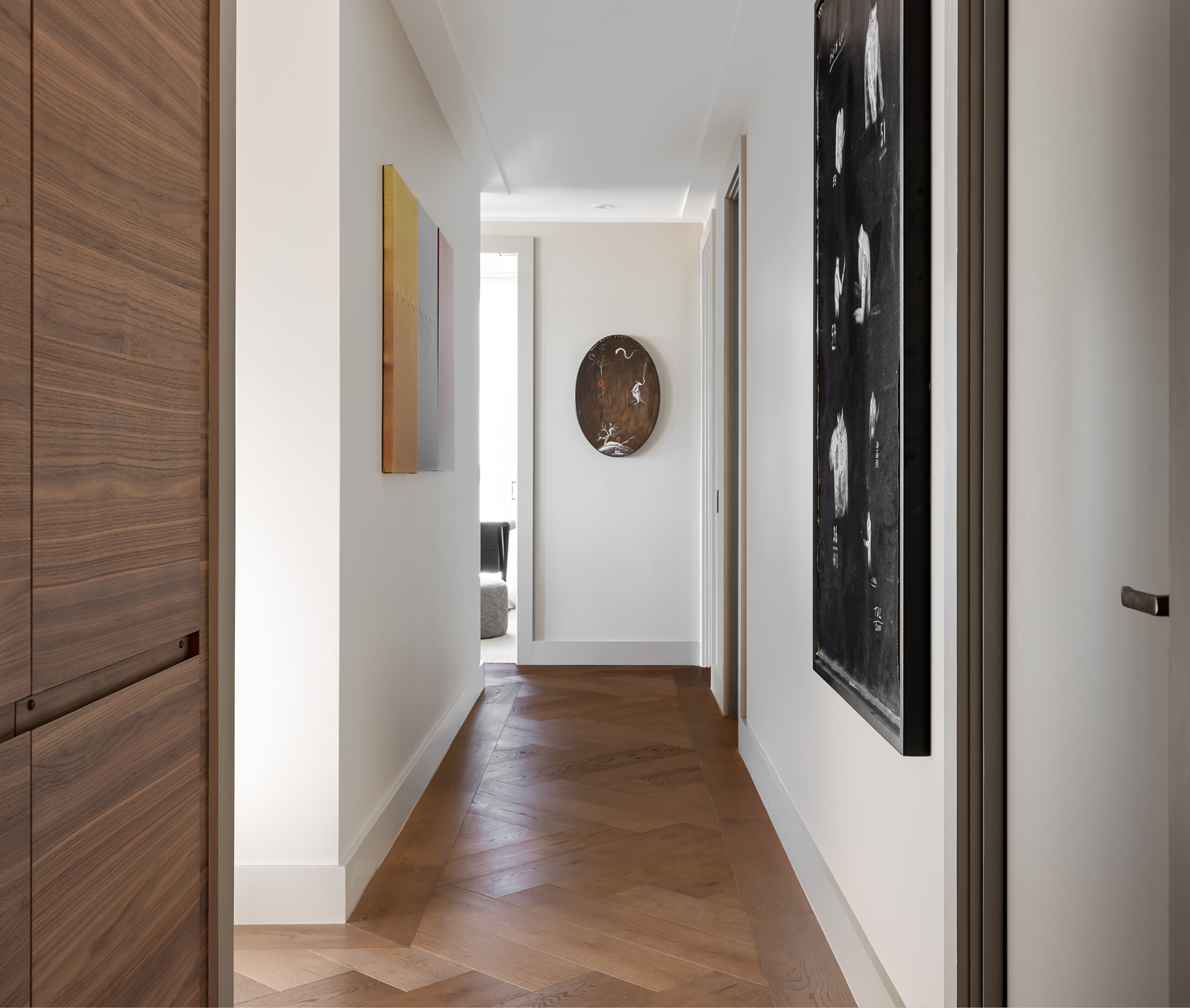 Apartment hallway featuring warm timber panelling, herringbone flooring, white walls and contemporary artwork.