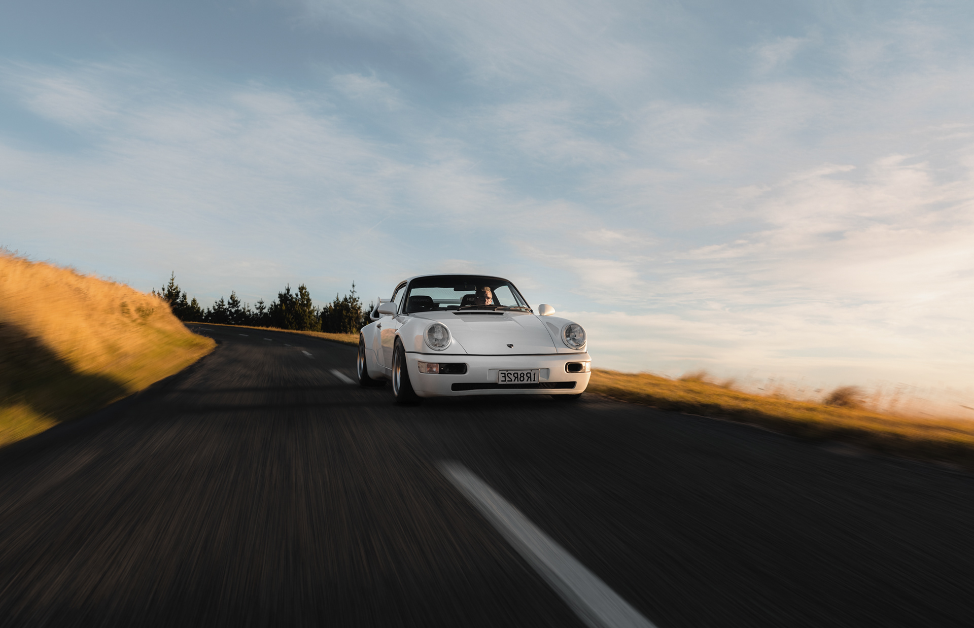 White classic Porsche 911 driving on a rural New Zealand road at golden hour