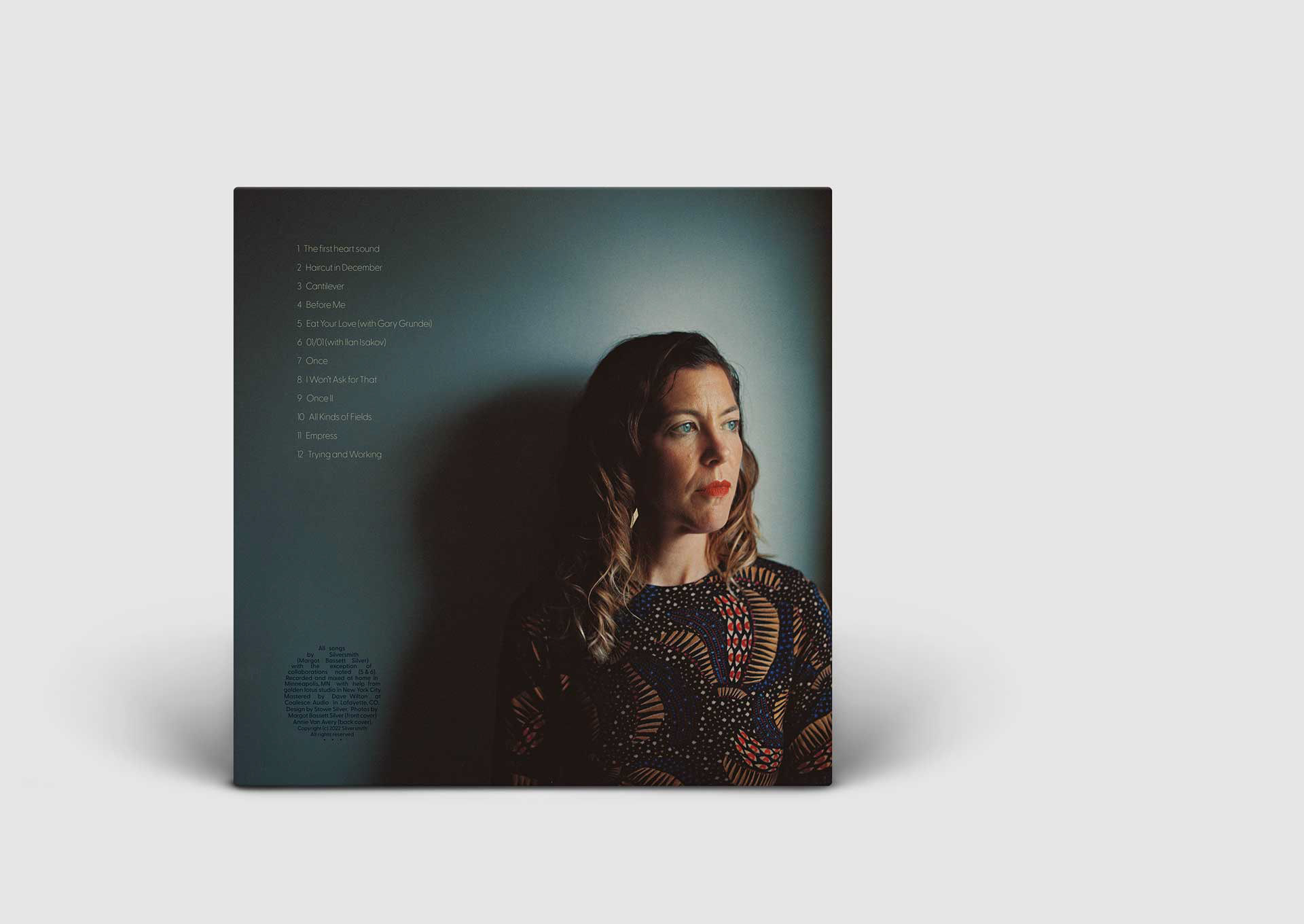The back cover of the album. It has a deep blue green background. A white woman with long brown hair is in the foreground, looking off to the side.