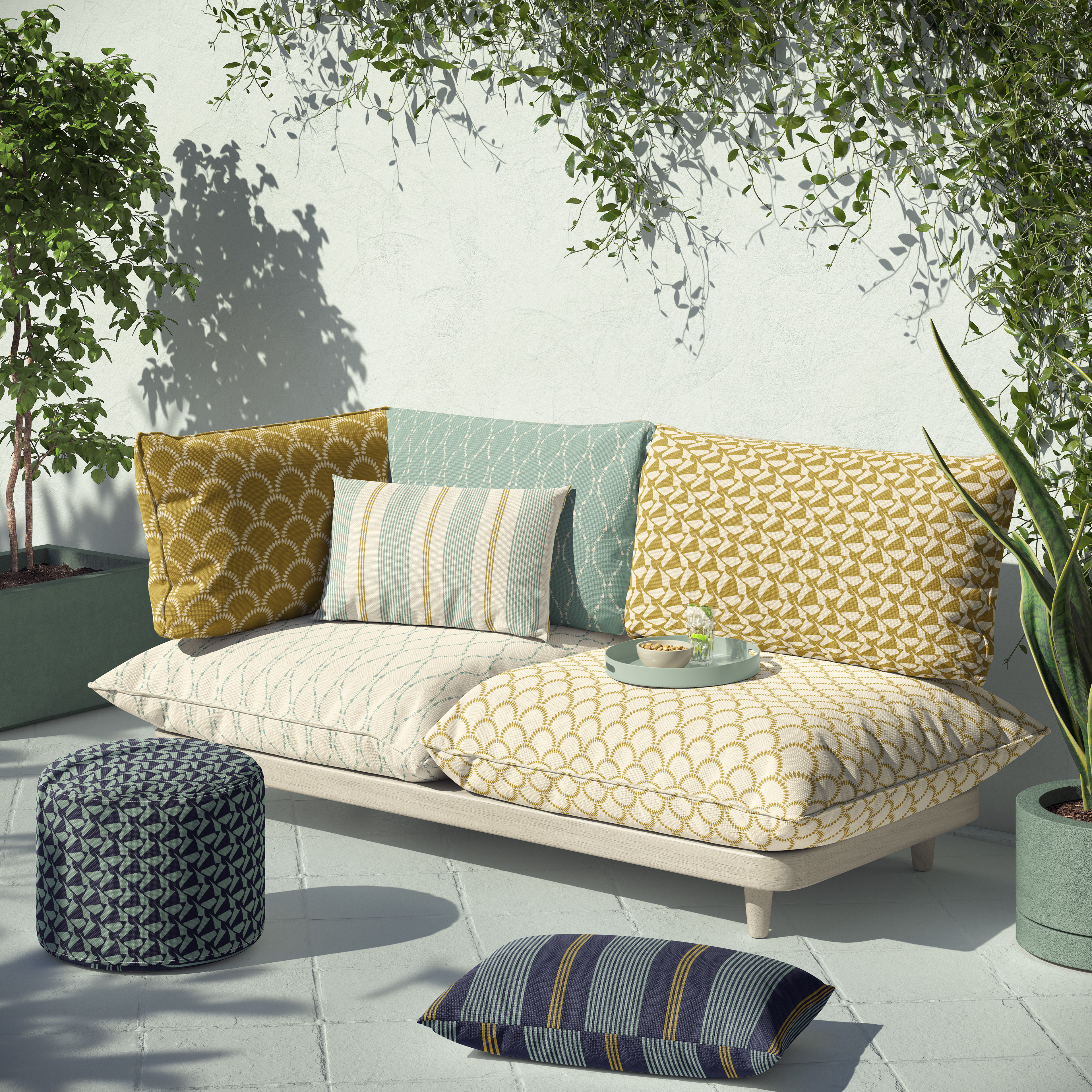A collection of colorful outdoor cushions and poufs showcasing geometric and floral patterns, styled in a bright patio setting with greenery.