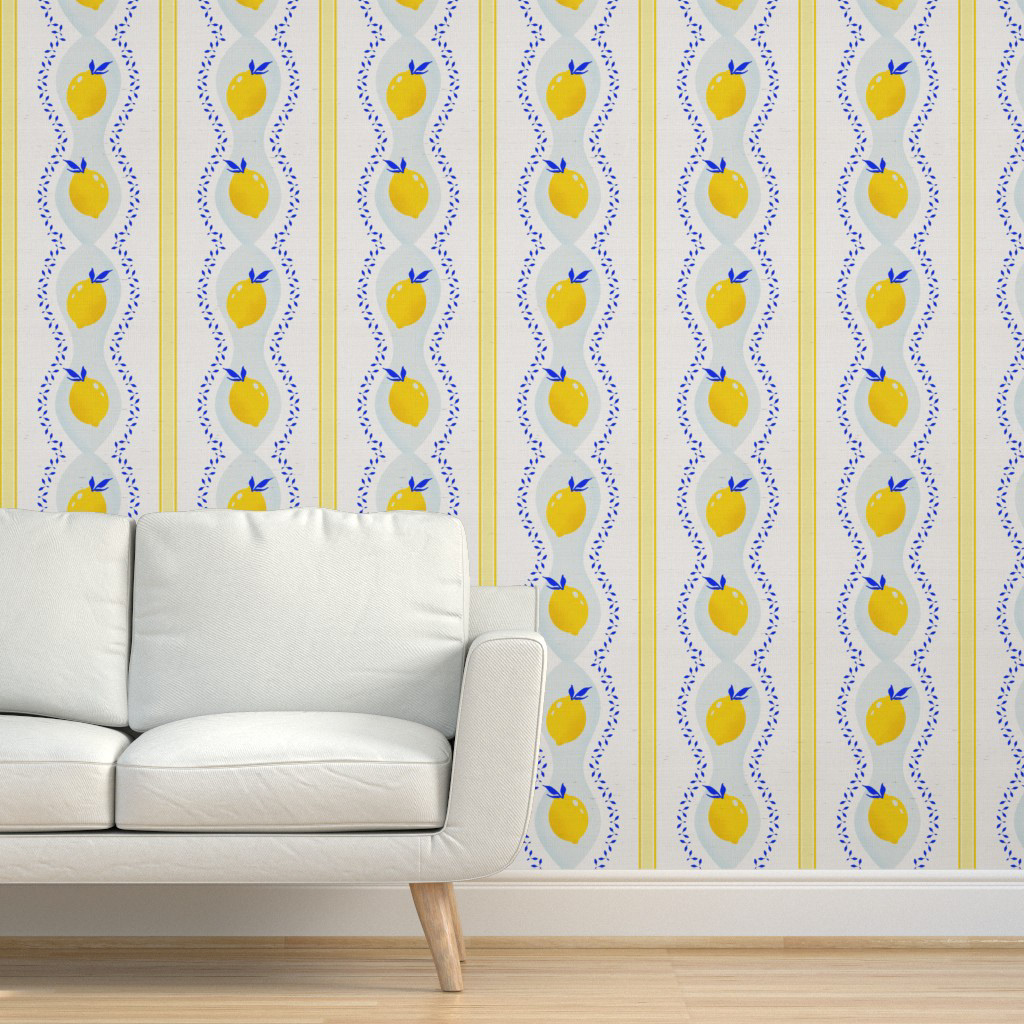 A modern farmhouse living room with a white sofa against a wallpapered wall featuring vertical stripes of yellow fruit and blue leaf patterns on a light background. The wallpaper is bright, fresh, and features a clean, repeating design with a fresh organic feel.