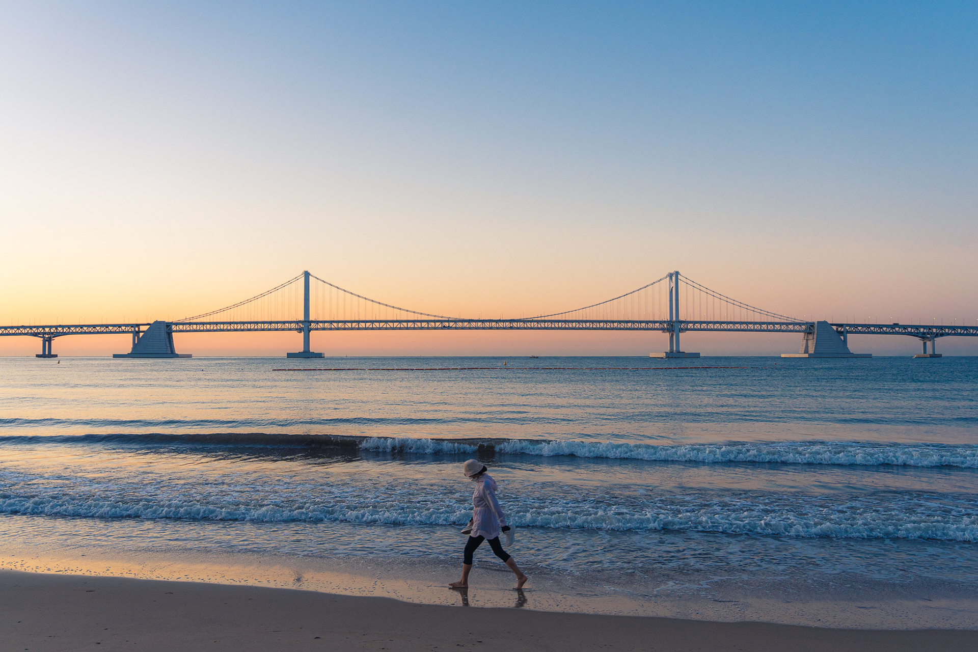 Woman walking on Gwangalli Beach - Busan, South Korea, during sunrise.