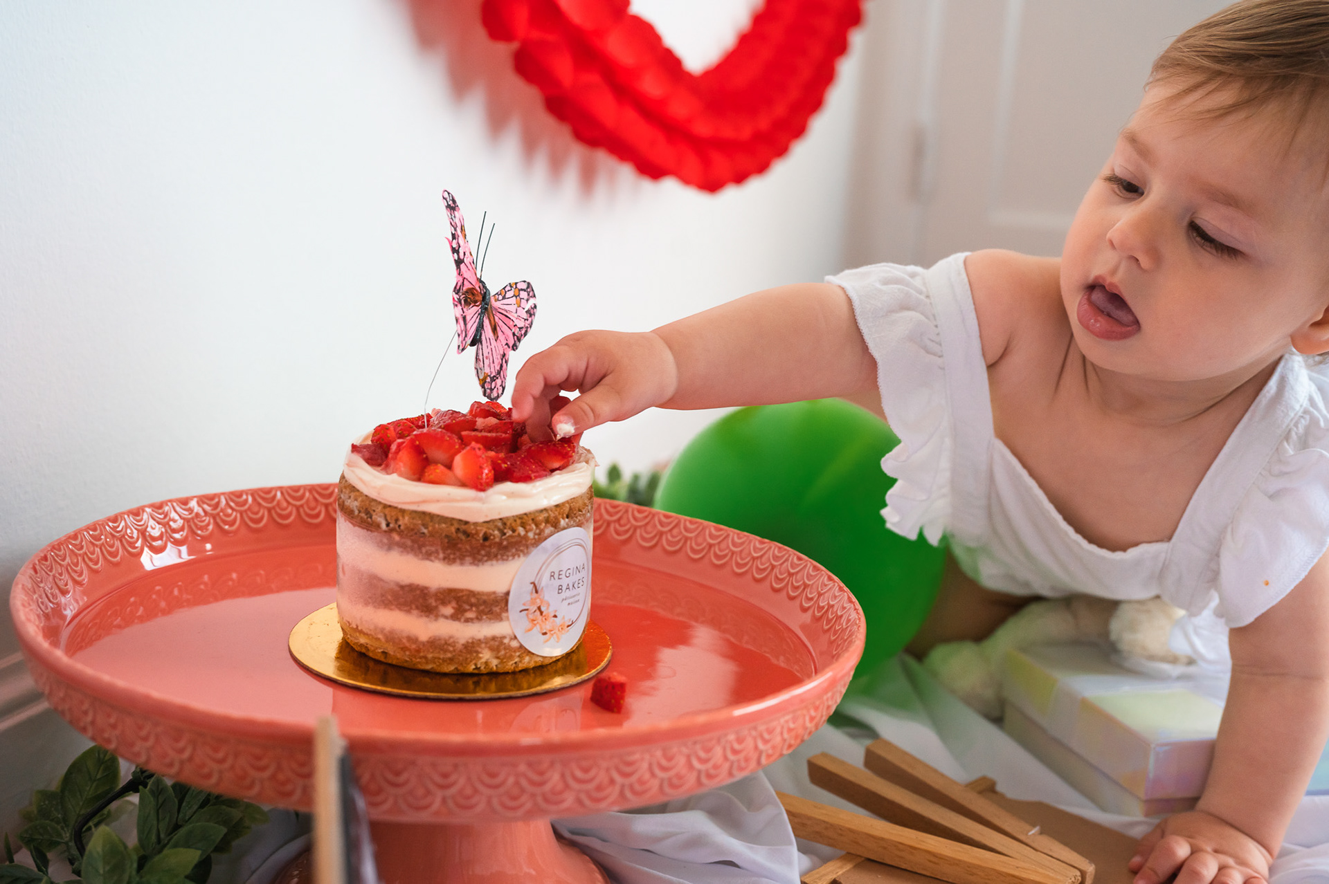 A baby admiring her strawberry-topped birthday cake.