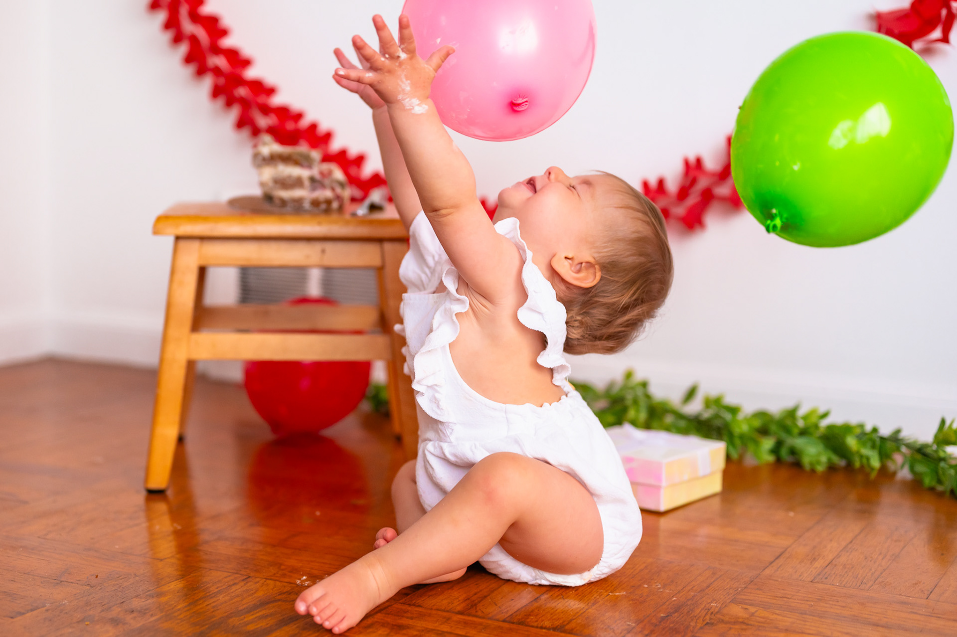 Newly minted one year old celebrating with balloons at her strawberry-themed cake smash!