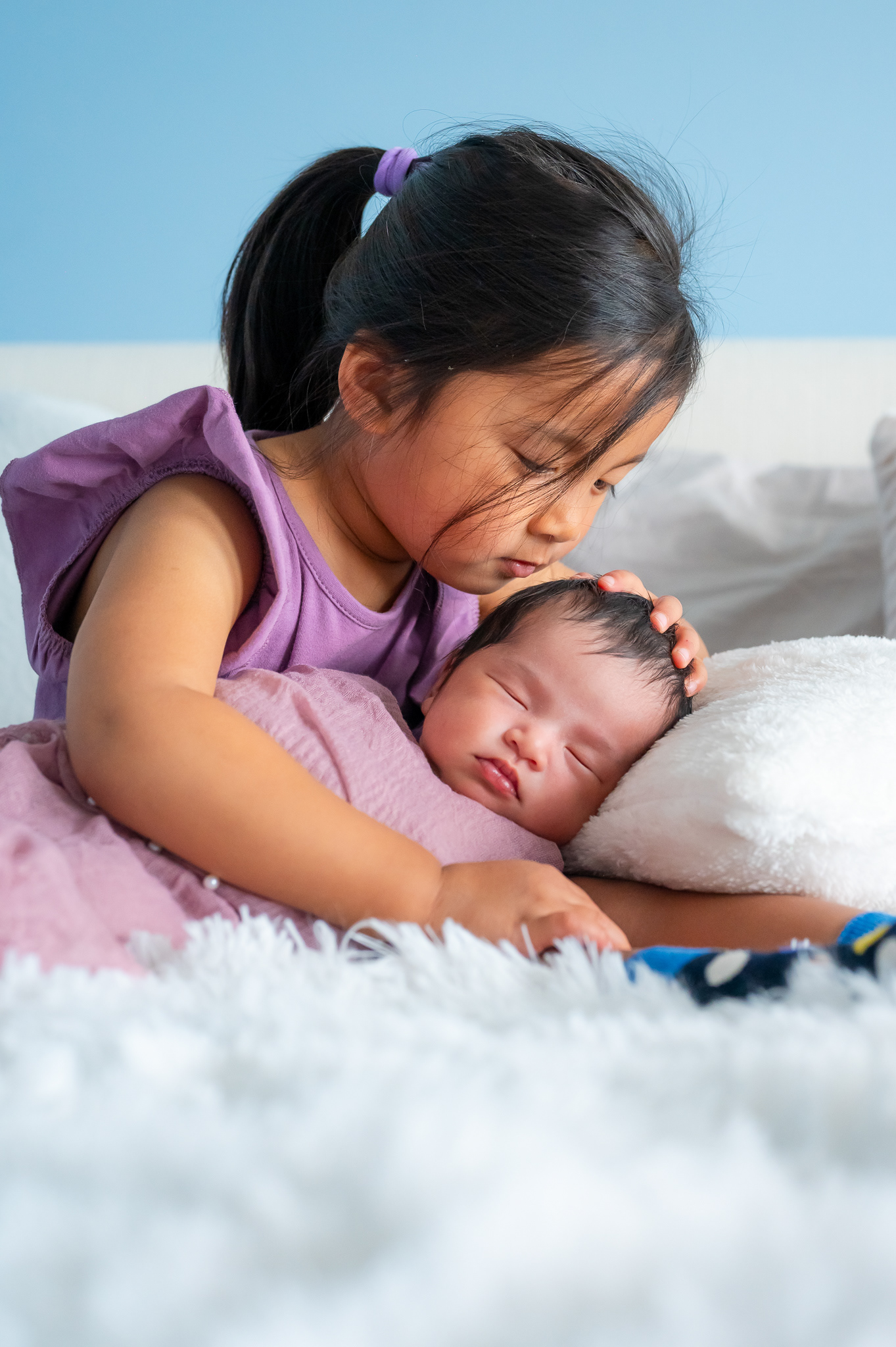 Big sister about to kiss her newborn sister on the head.