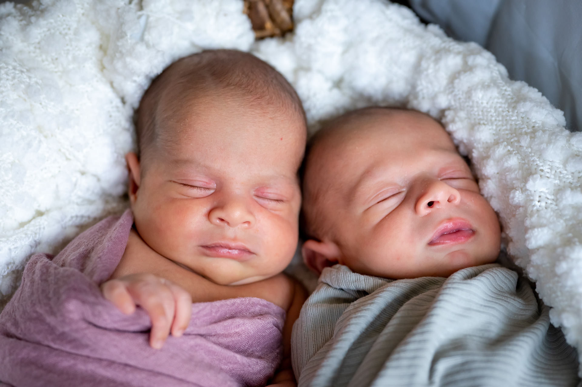 Newborn twin babies sleeping in a basket.