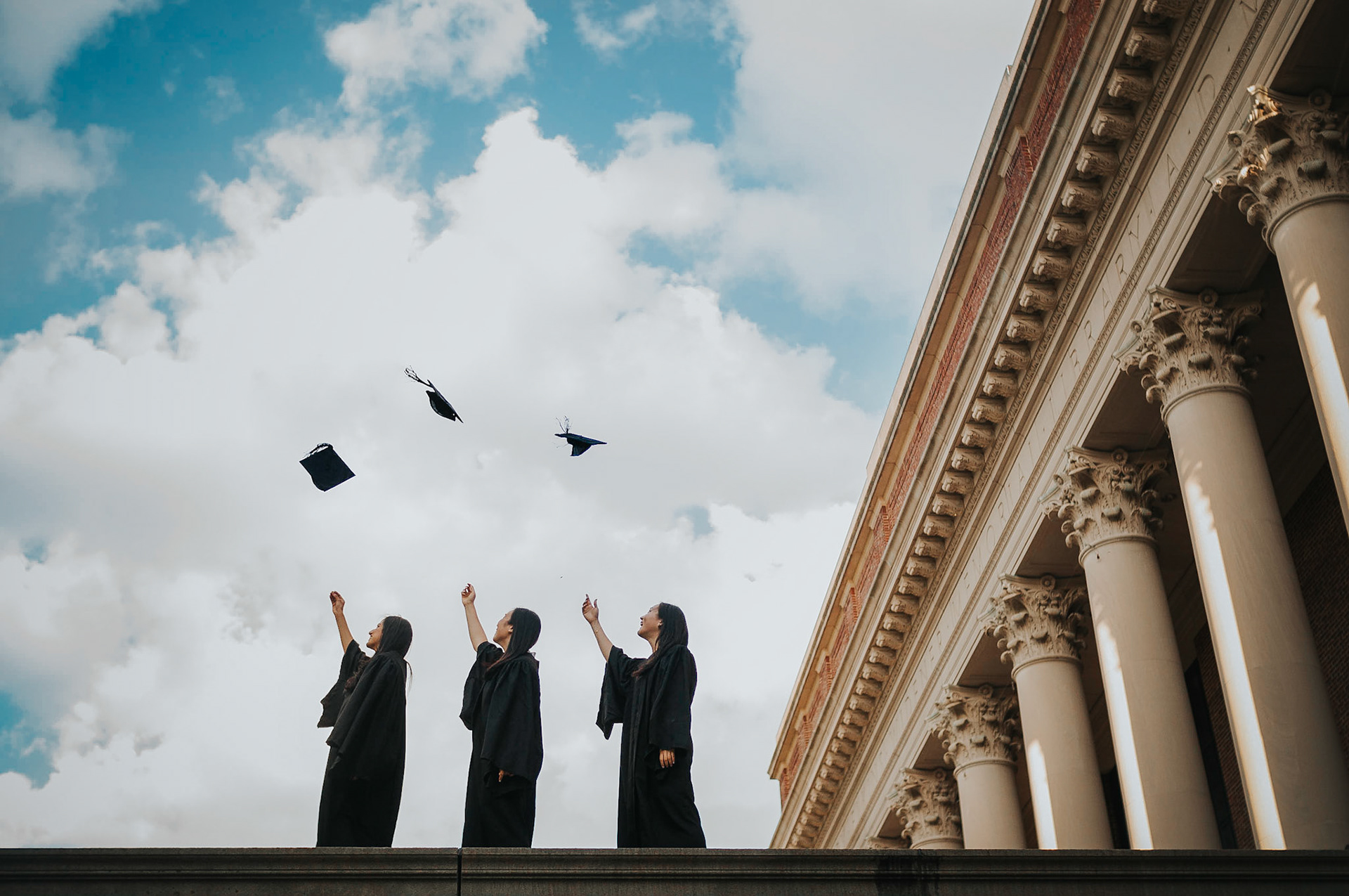 Three undergraduates celebrate graduating from Harvard University next to Widener Library. Photo taken by Dean Shu.
