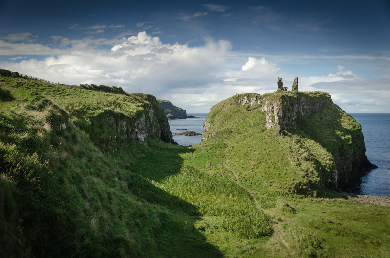 Ruins of Dunseverick Castle sit on a tall, grassy, rocky headland overlooking the sea.