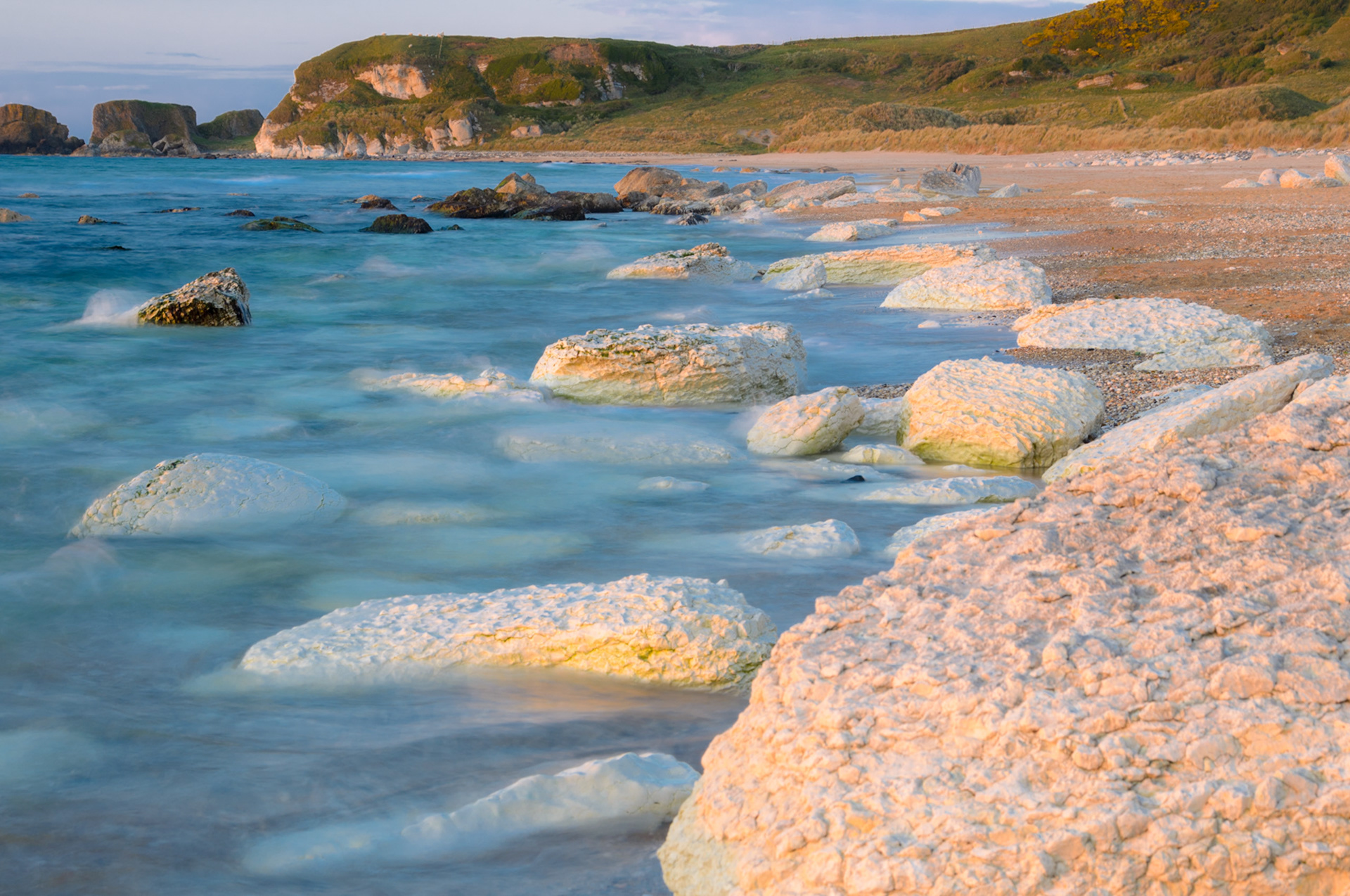 Whitepark Bay At Sunset: Long exposure view of Whitepark Bay showing smooth water, rocks, and warm sunset light on the horizon.