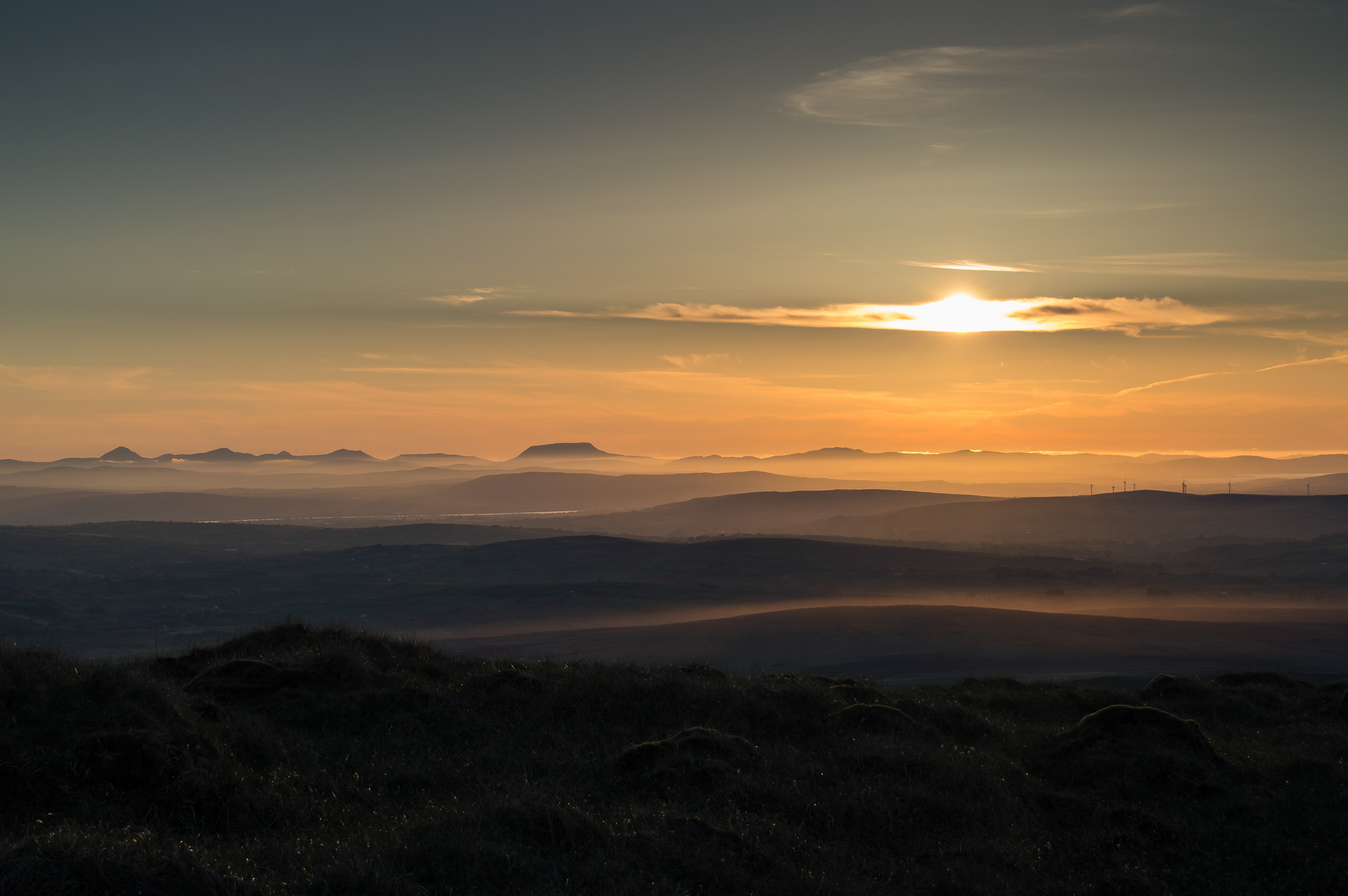 Spectacular sunset over Mullaghclogha Mountain and layered hills, with a golden and hazy sky.