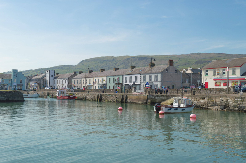 Carnlough Harbour and stone pier with small boats. View of the village and hills beyond.