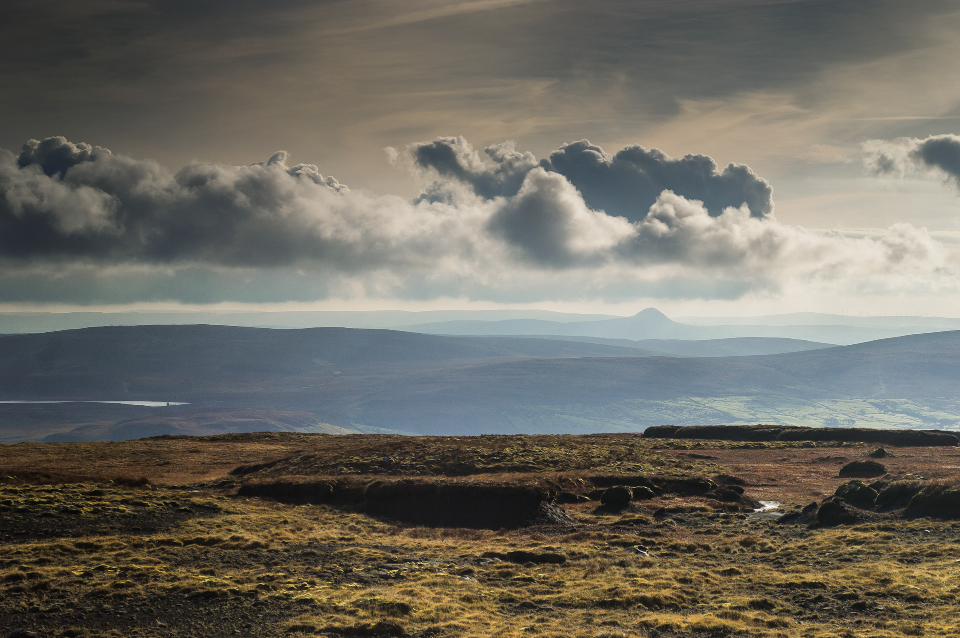 The Summit of Trostan: Wide open summit plateau covered in peat bog and heathland under dramatic clouds, with Slemish on the horizon.
