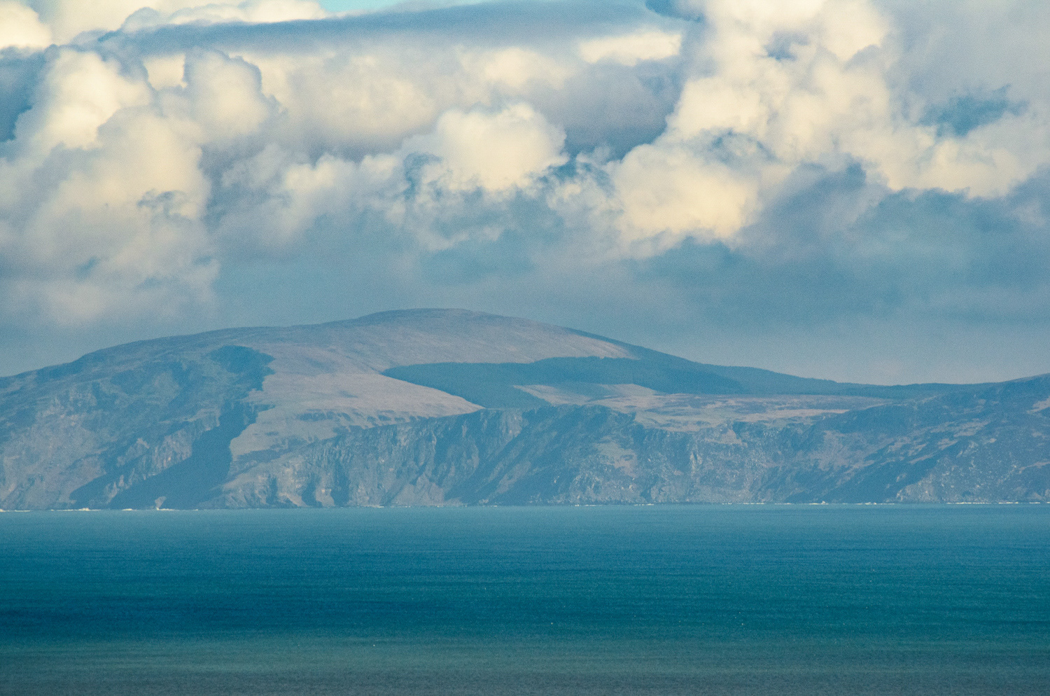 Distant view of the Scottish island of Kintyre across the sea from Murlough Bay. Dramatic clouds hover over the cliffs.