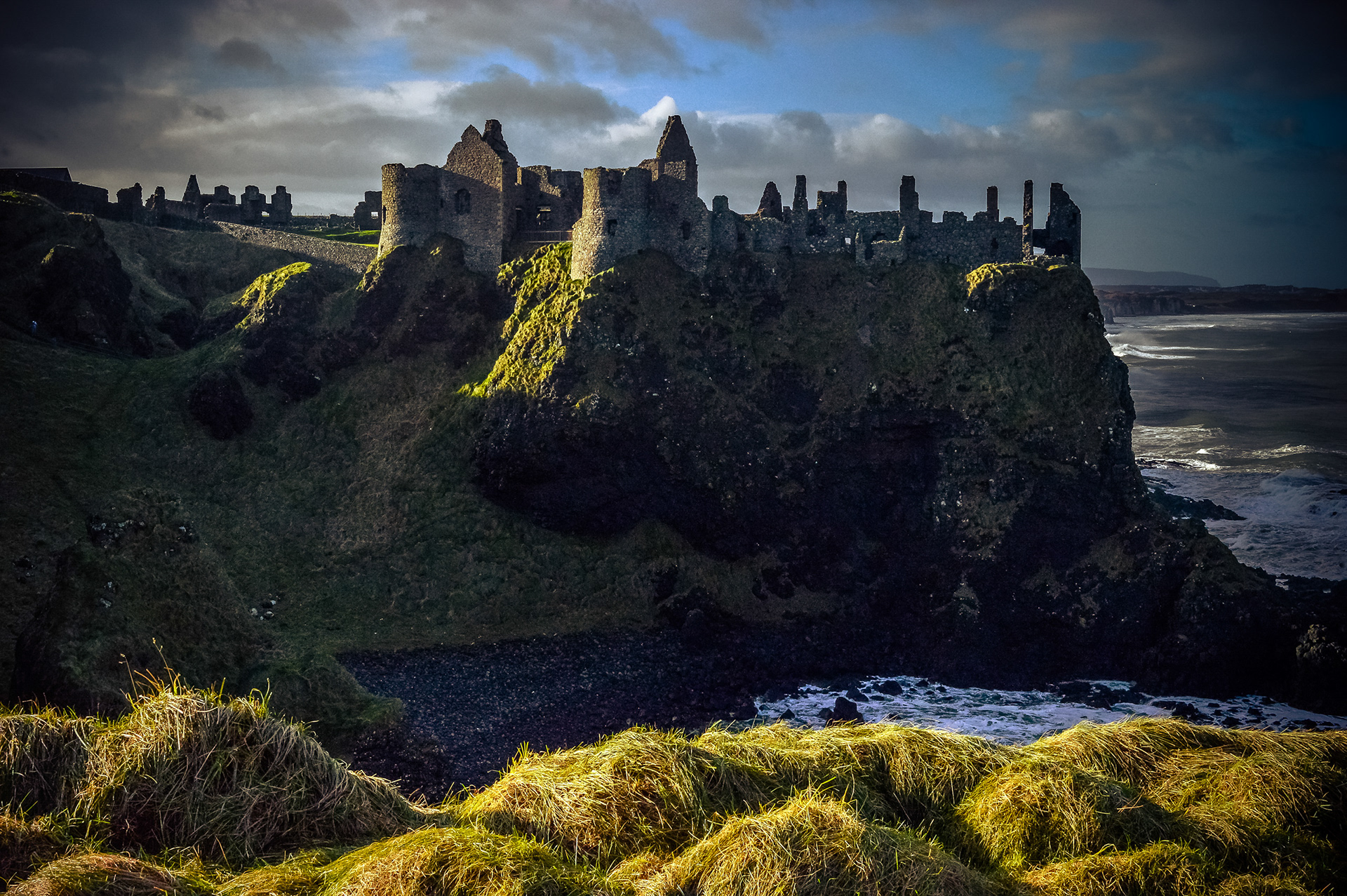 Ominous Fortress: Dunluce Castle perched on a cliffside under a dark sky with dramatic shadows and light.