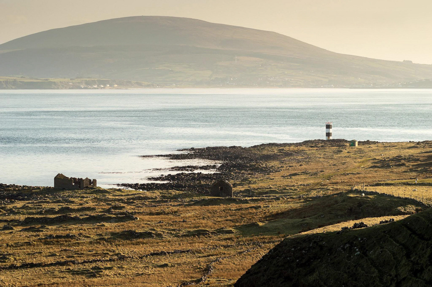 The lighthouse structure and ruins at Rue Point, Rathlin Island, at sunset. The land is low and covered in dry grass.