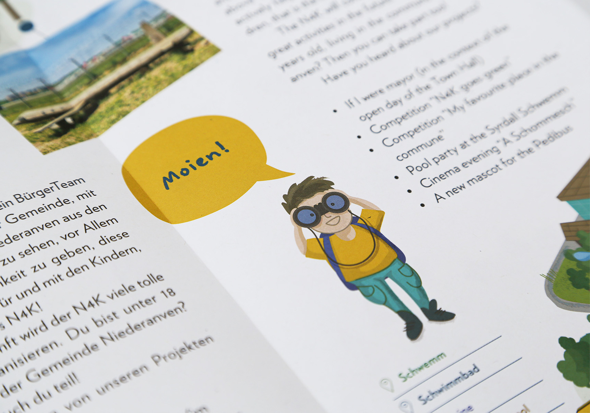 The image shows a section of the layout for the children's map of Niederanven. It features an illustration of a boy looking through binoculars and saying “Moien!” Text can be seen around the edge.