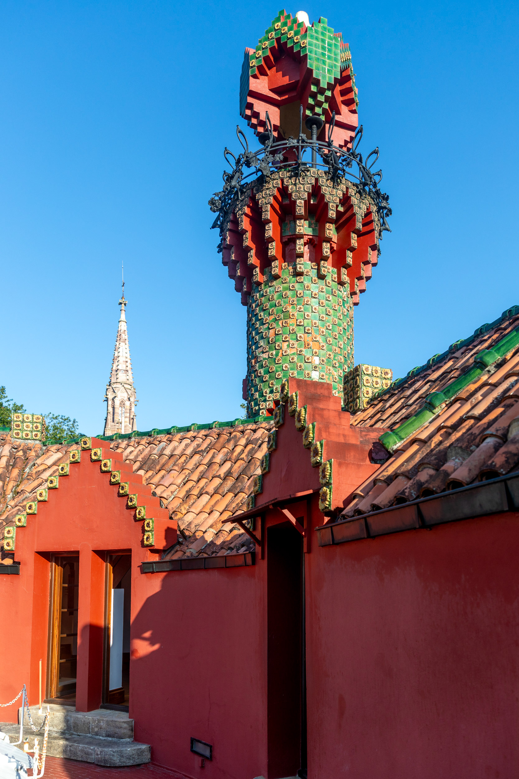 Twenty metres of tiled tower, seen from the roof terrace. The form is generally described as a minaret, and the building belongs to Gaudí's orientalist period of 1883–88.