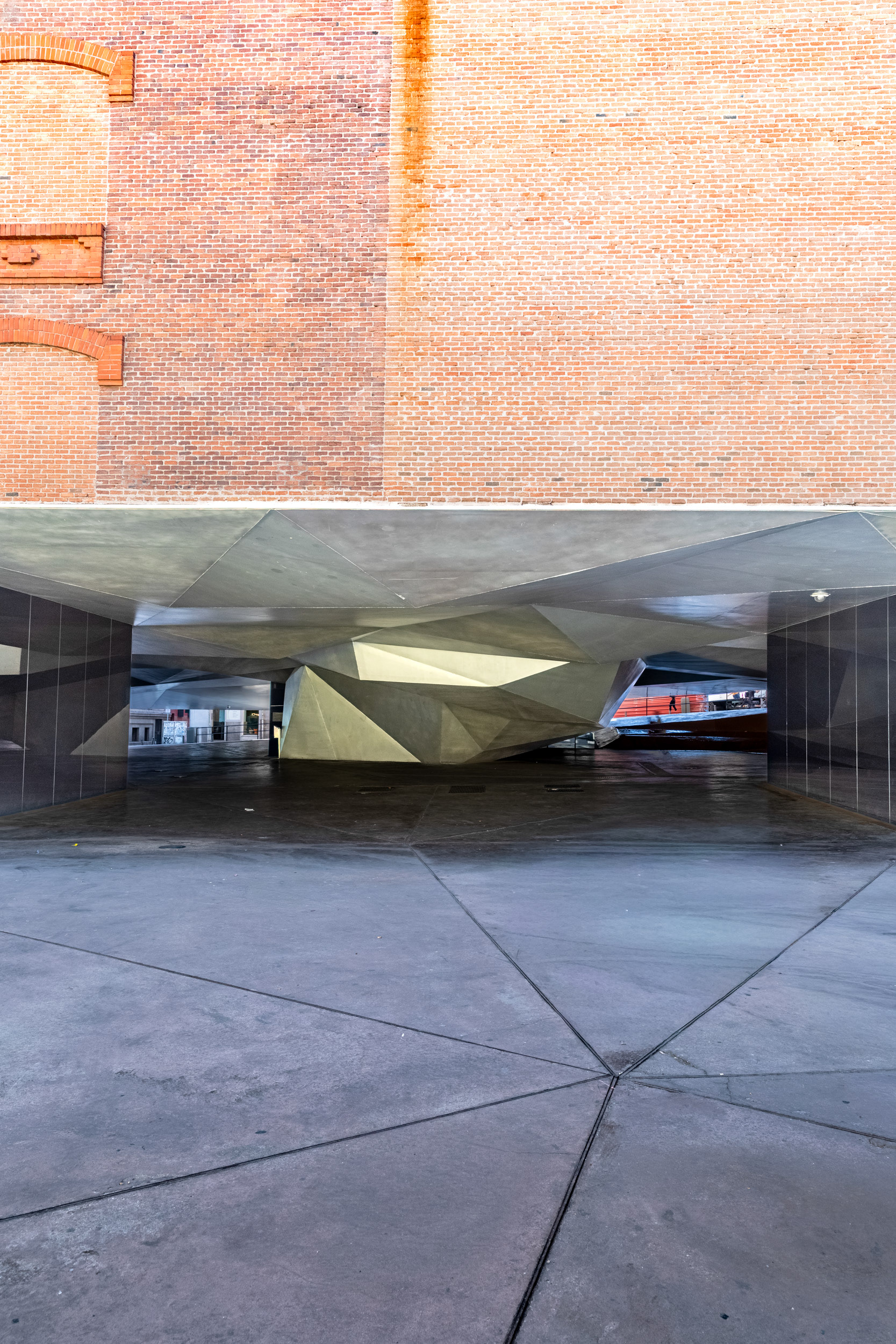 The faceted underside of the entrance canopy, seen from Paseo del Prado, beneath the original brick facade.