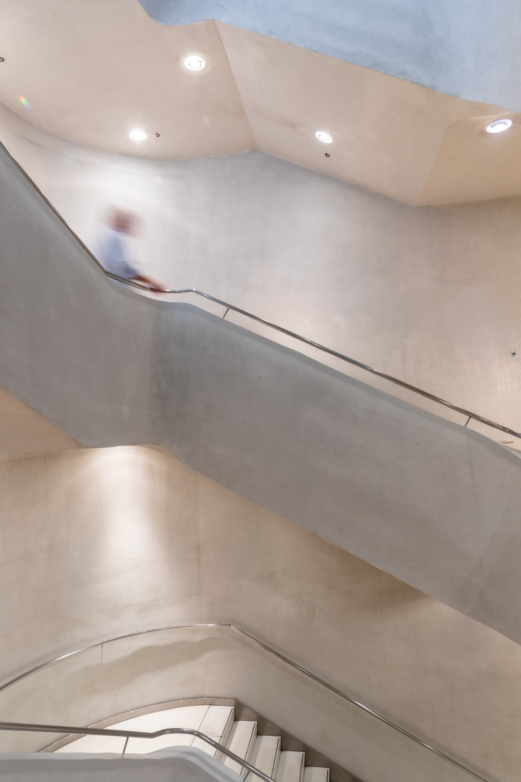 A visitor on the same staircase, its walls cast in a continuous curve rather than straight flights.
