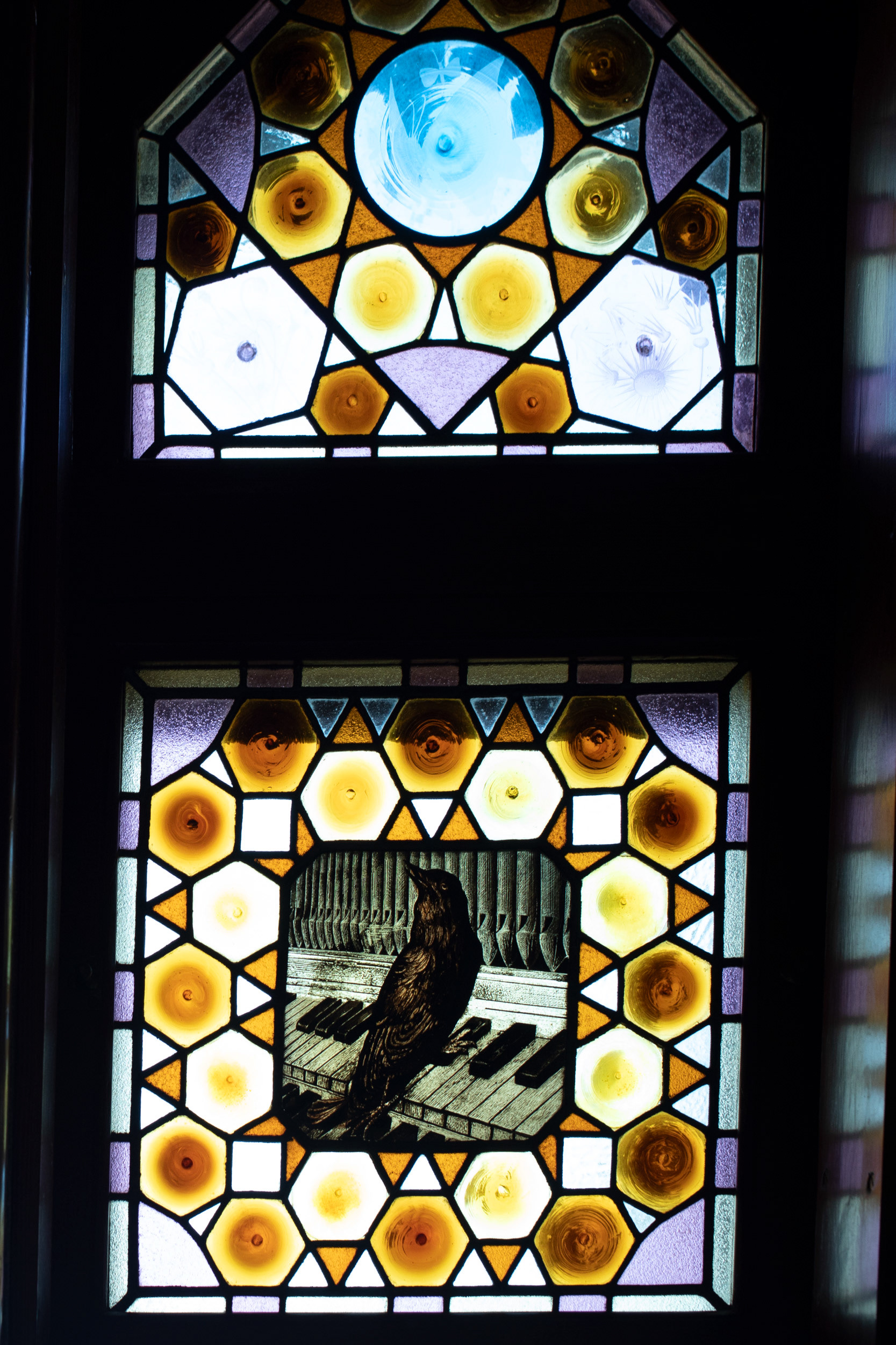 A stained-glass panel: a bird on a piano keyboard. Díaz de Quijano was an amateur musician.