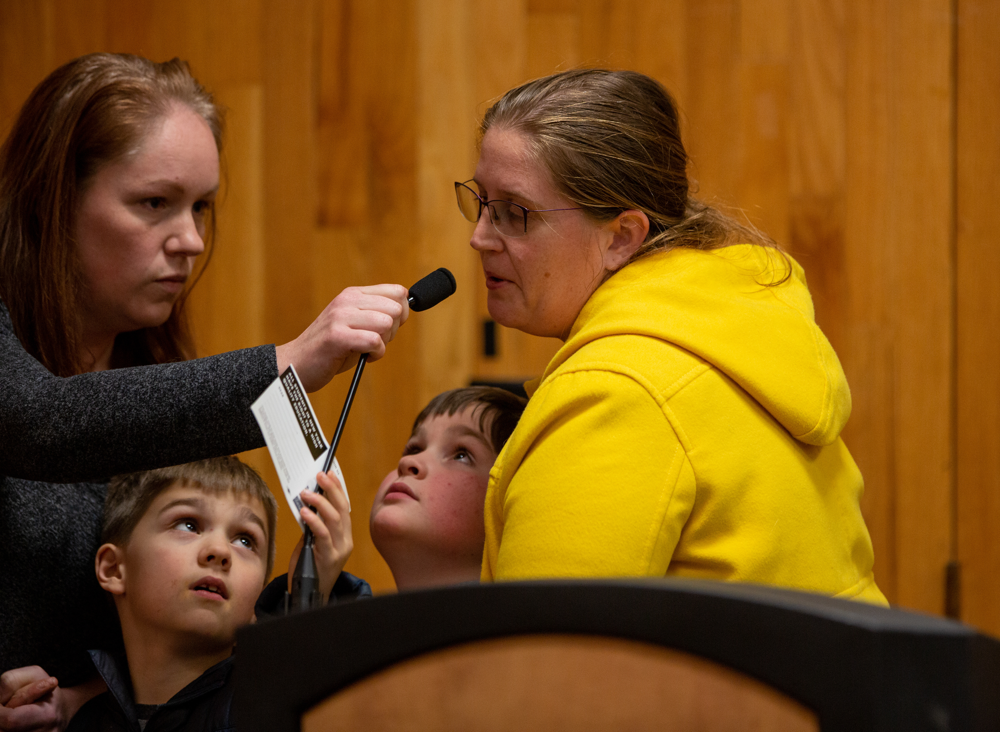 A mother and her two sons speak with a special education teacher at the board meeting about how teachers are needed to help students.