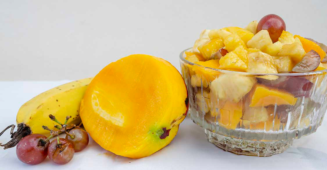 A fruit dish beside beside whole fruits and  a half mango. Link to Popular Photos.