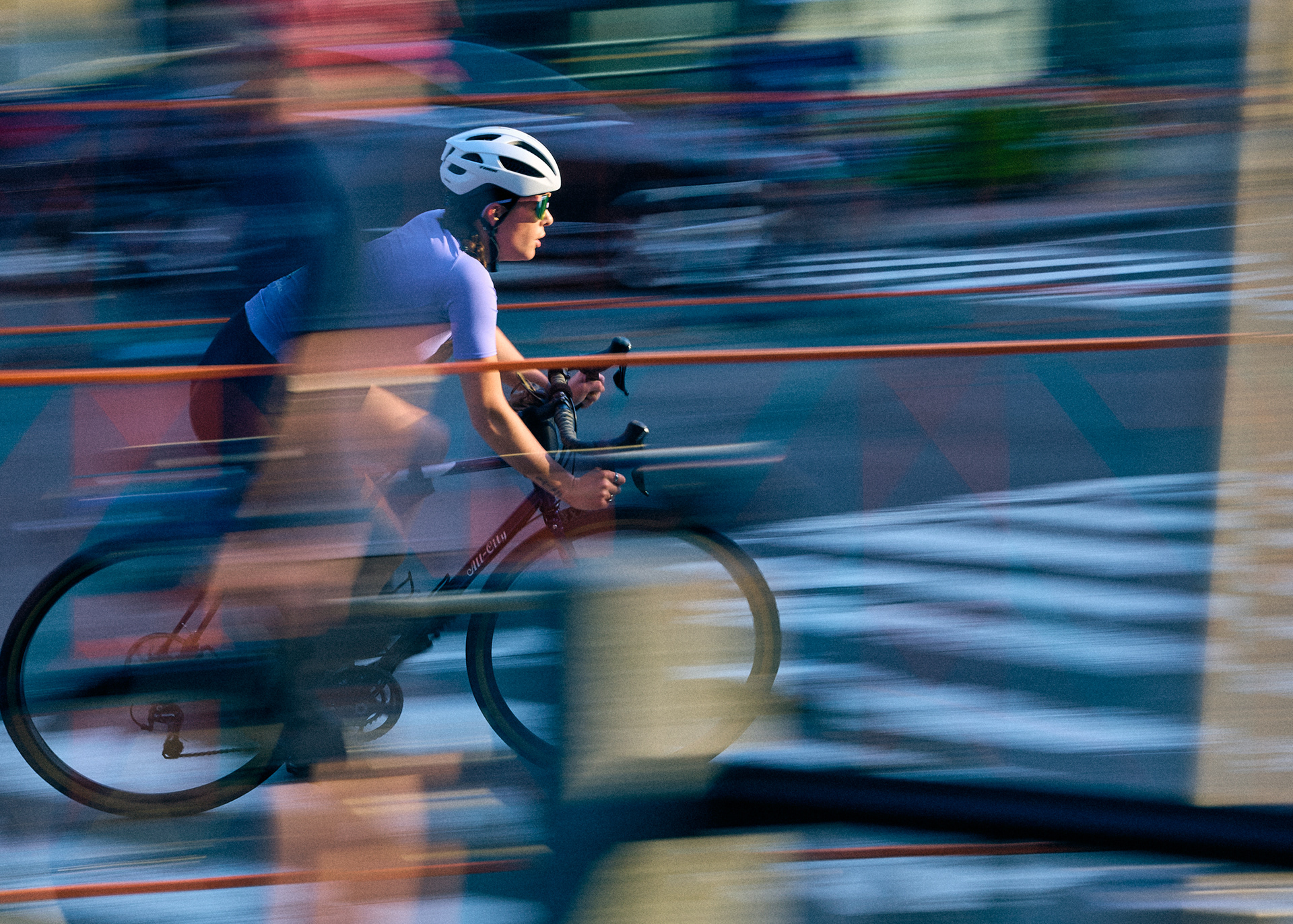 Cyclist in a white helmet and lavender jersey seen through layers of motion blur