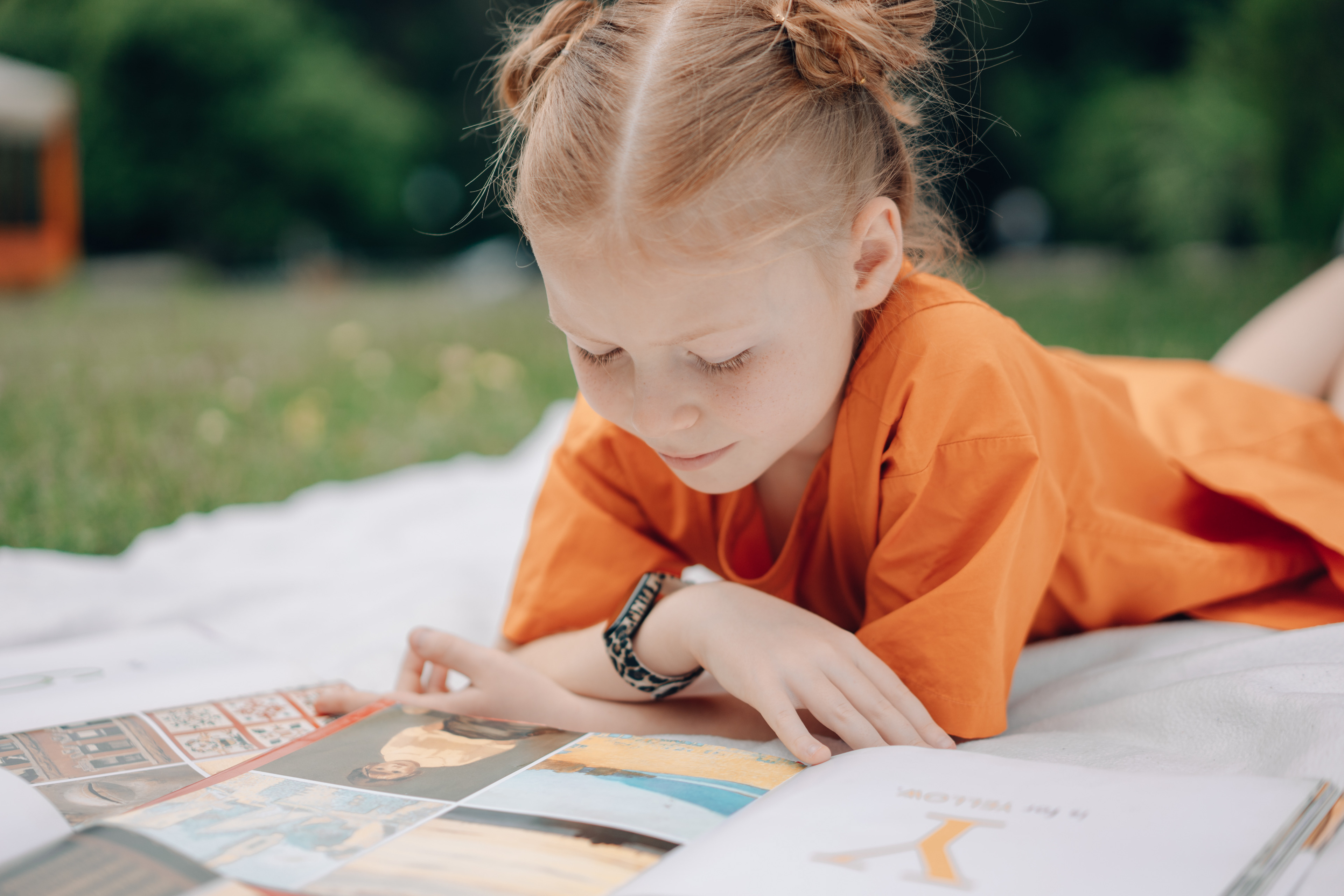 sunny day in the park with red haired girl reading book on blanket