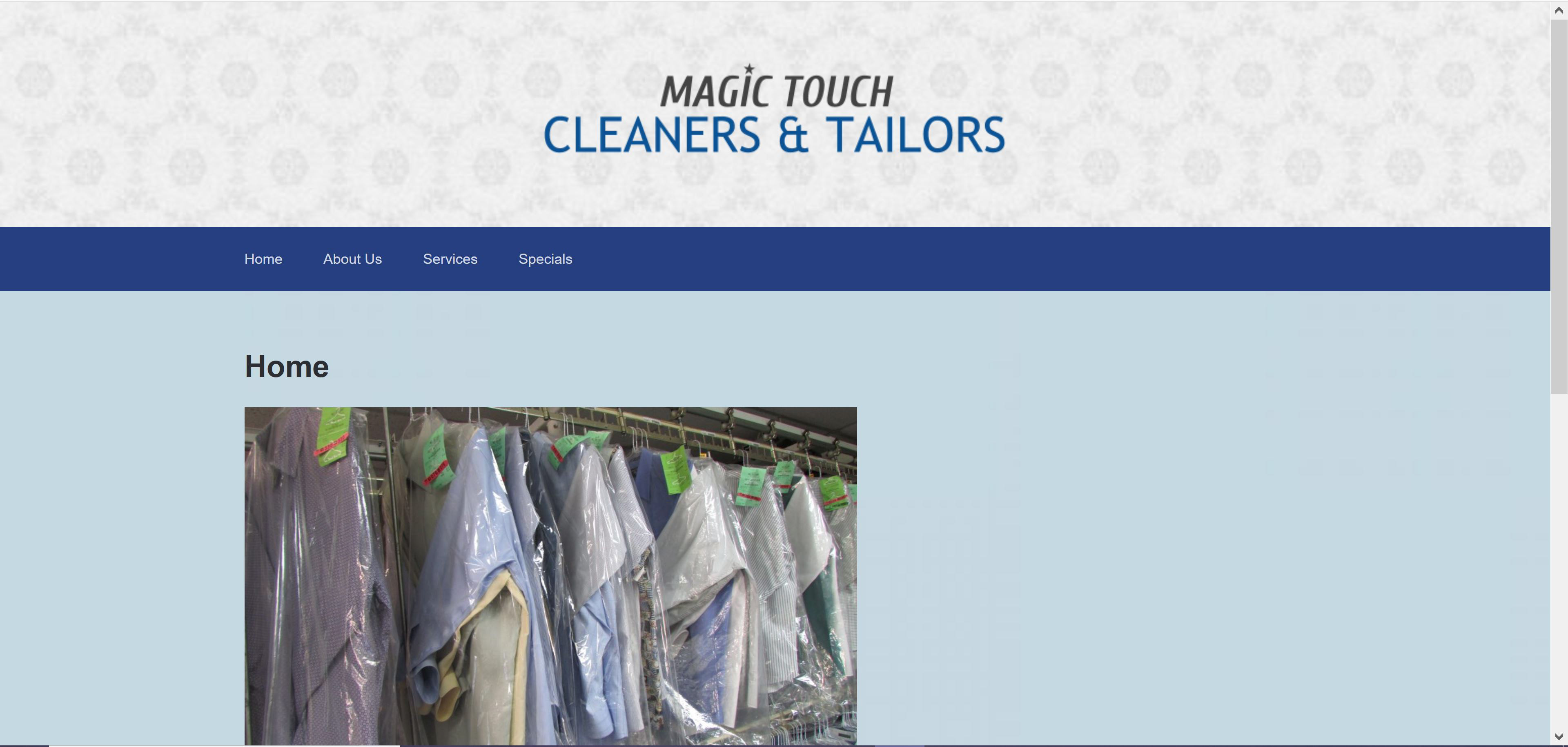 An image of Magic Touch's previous website. There is a grey, subdued, patterned banner at the top with the text "Magic Touch Cleaners & Tailors" centered over it in grey and blue text. Underneath it, is a plain, solid, blue navigation bar directing the user to different pages on the site. Below that, is the word "Home" on top of an image of recently cleaned clothing, hanging from a rack in the store. The home page is over a light blue background.