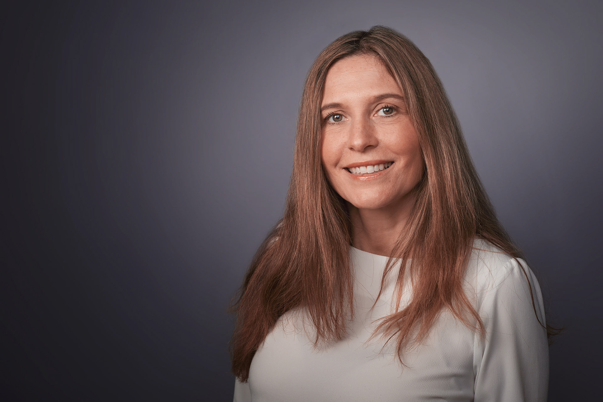 Professional business headshot of a smiling woman in a white blouse against a dark background, photographed in Cambridge for personal branding.