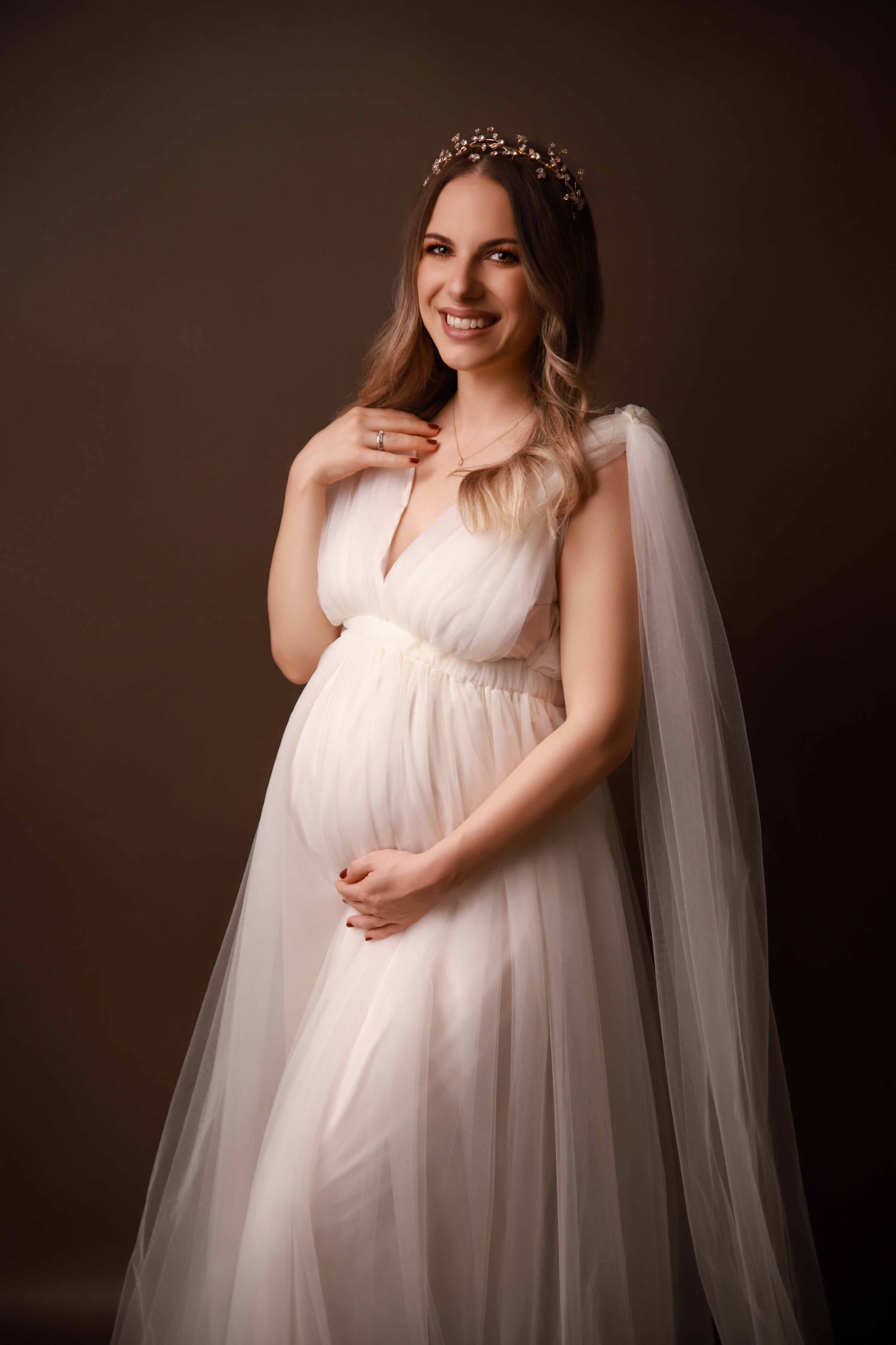 Schwangere Frau trägt ein Schönes weissßen kleid aus Tüll mit einer Krone in einer umwerfenden Pose - Babybauschshooting