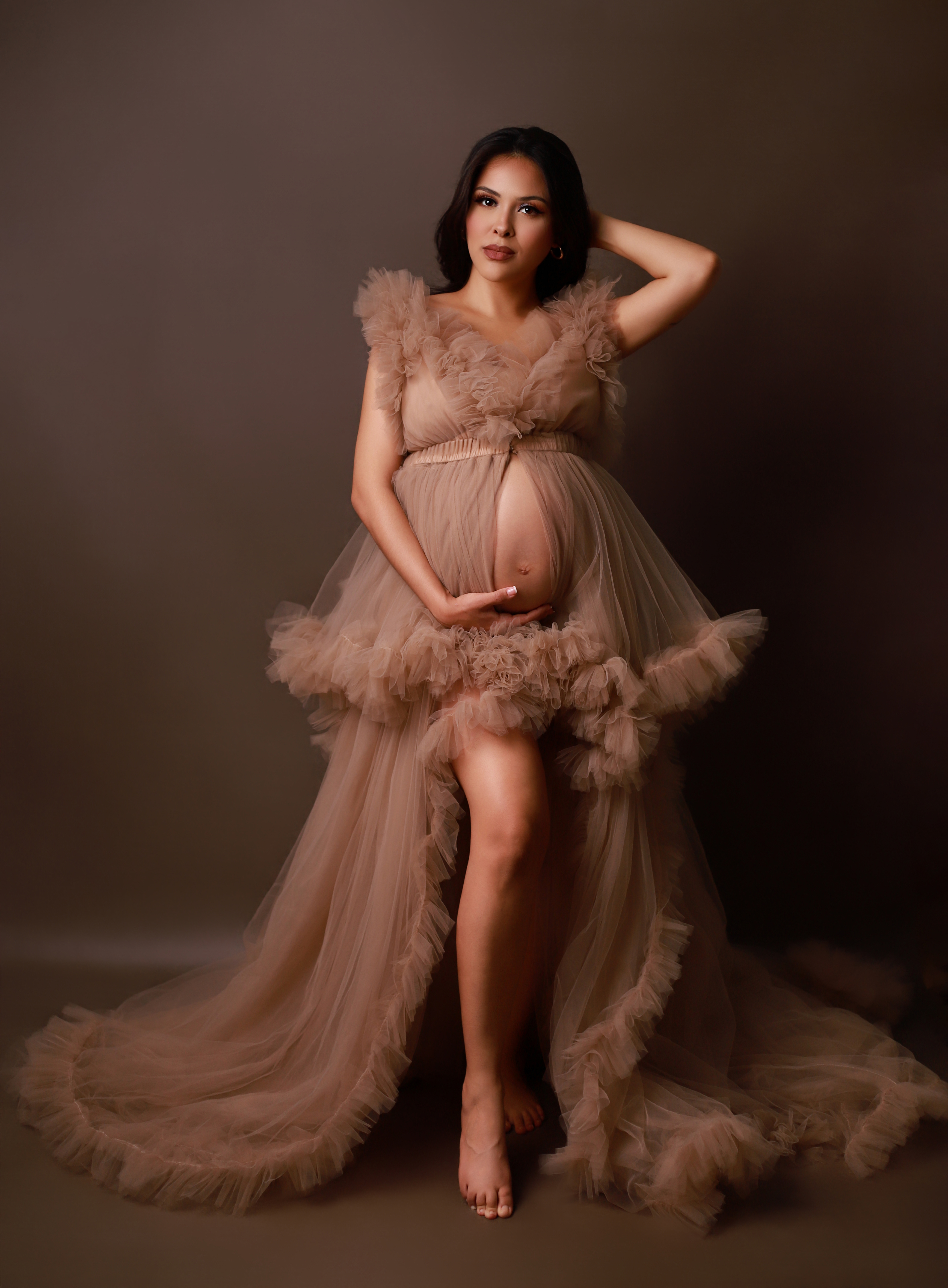 Schwangere Frau in einem beigen Kleid hält ihren Babybauch - Schwangerschaftsshooting